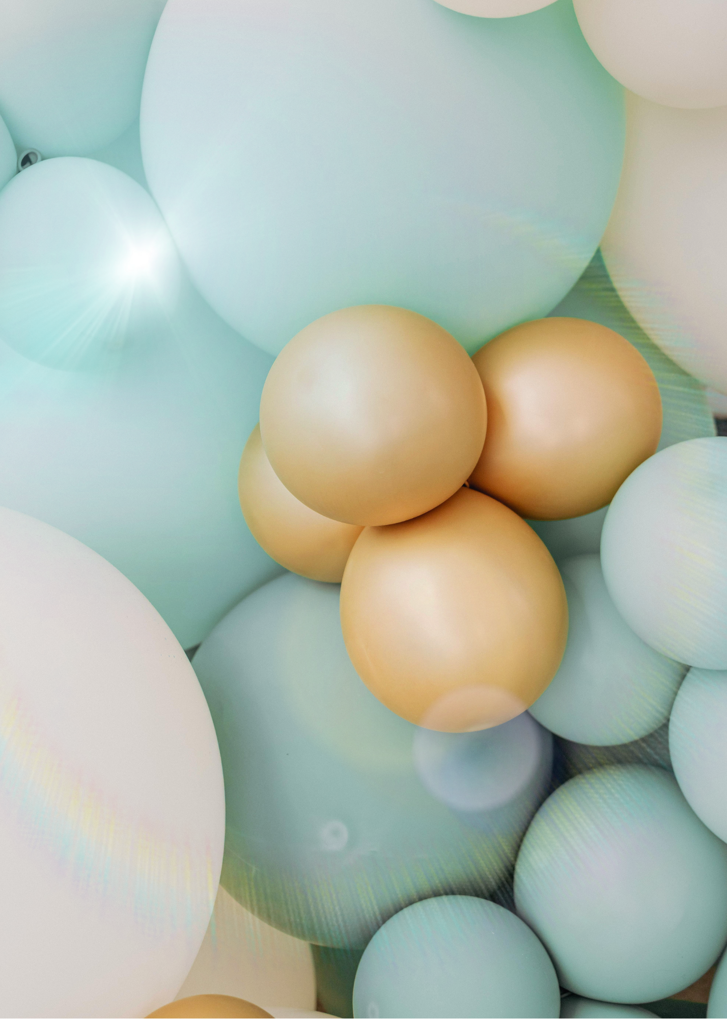 A collection of pastel-colored balloons in shades of light blue, cream, and pale yellow, overlapping each other.