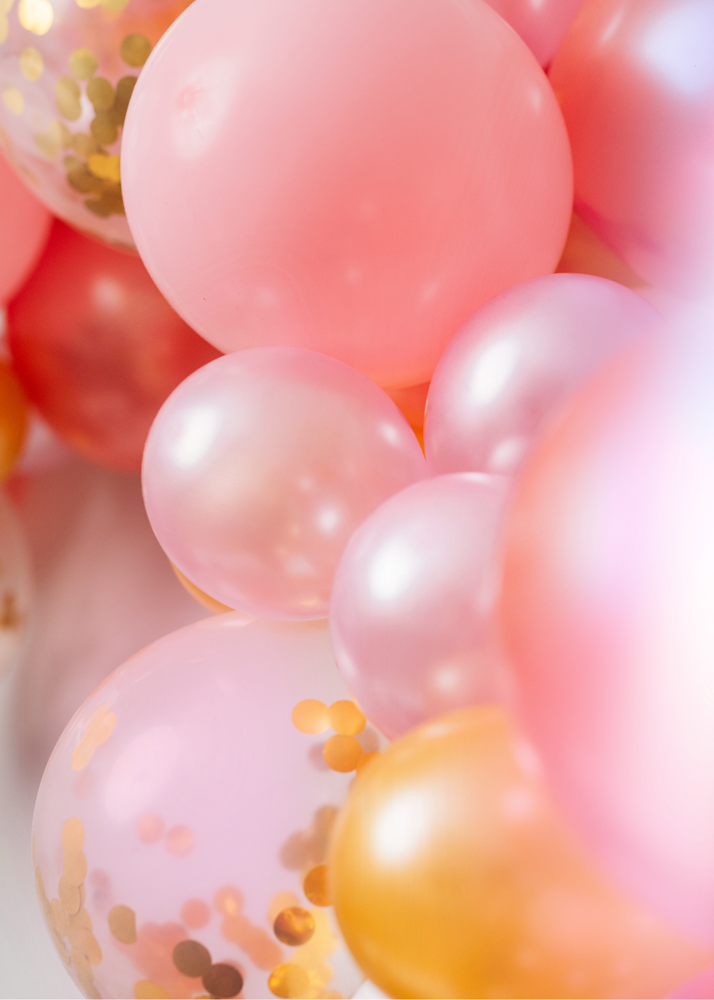 Close-up of pink, gold, and peach-colored balloons, some with gold confetti inside, at a celebration or party.
