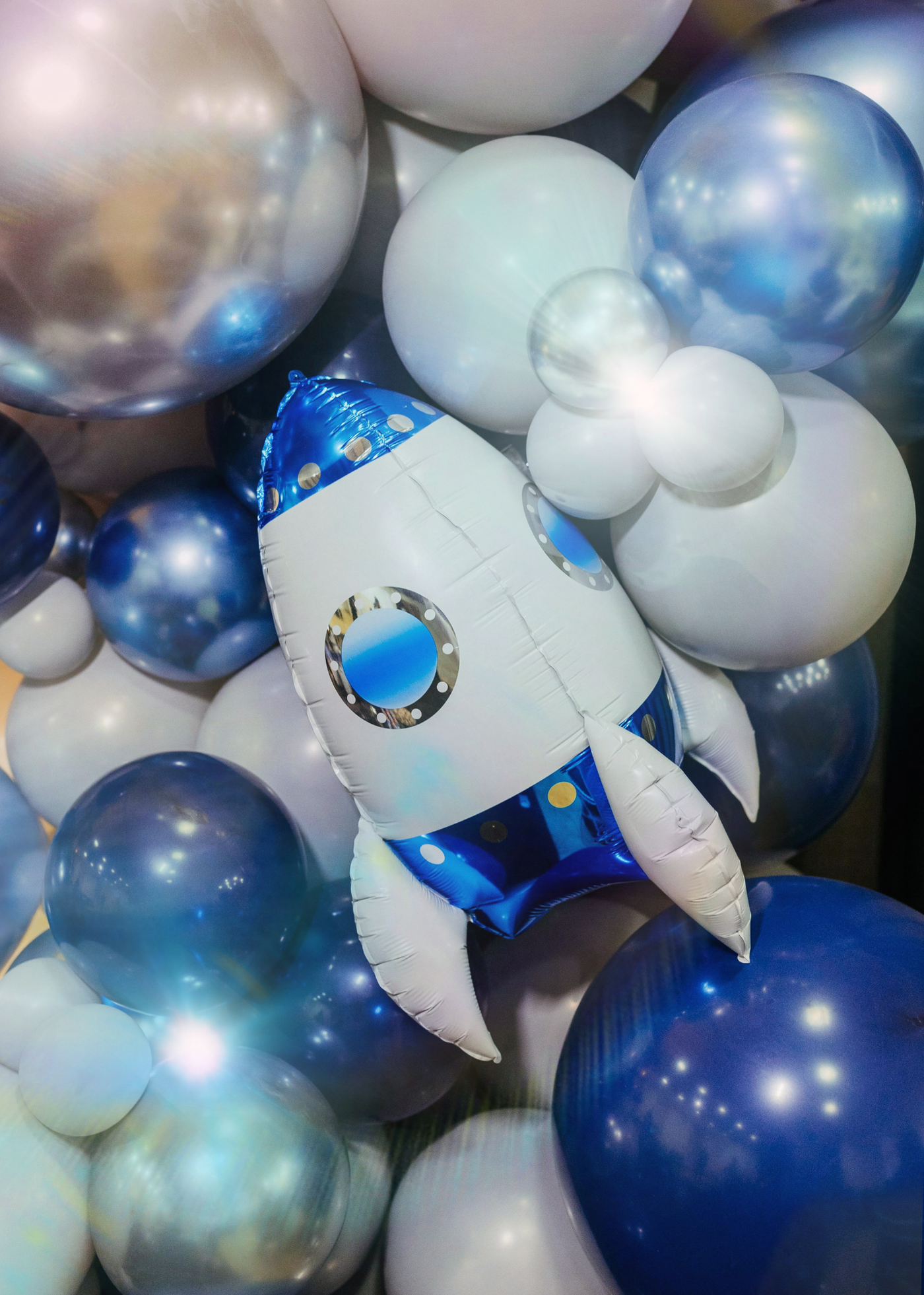 Collection of blue, white, and metallic balloons with an astronaut-shaped balloon among them.