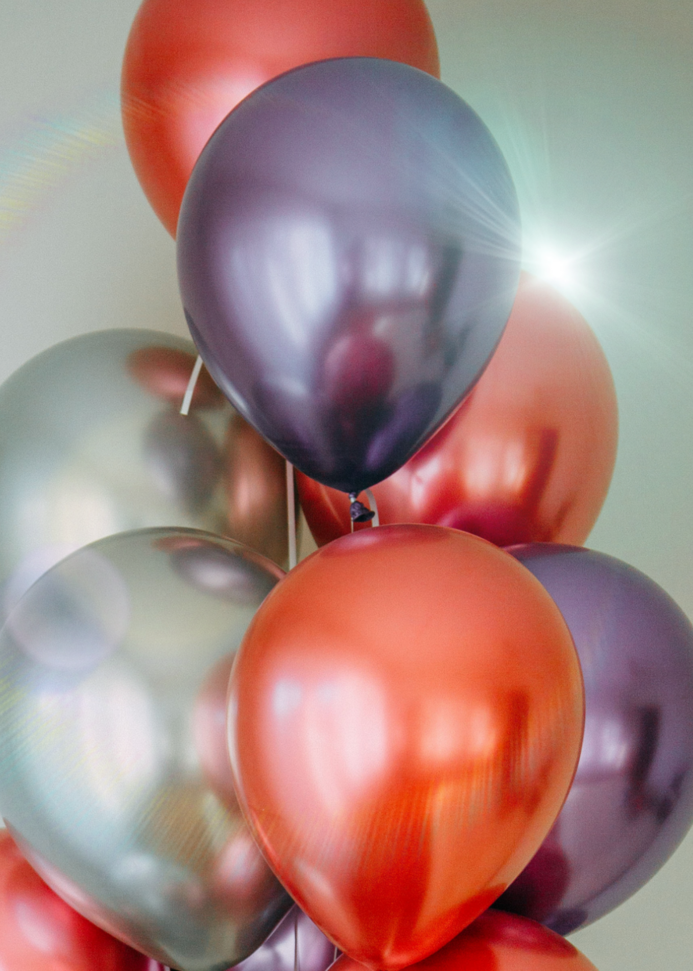 A cluster of colorful balloons, including red, purple, silver, and black, with a bright light reflection on the purple one.