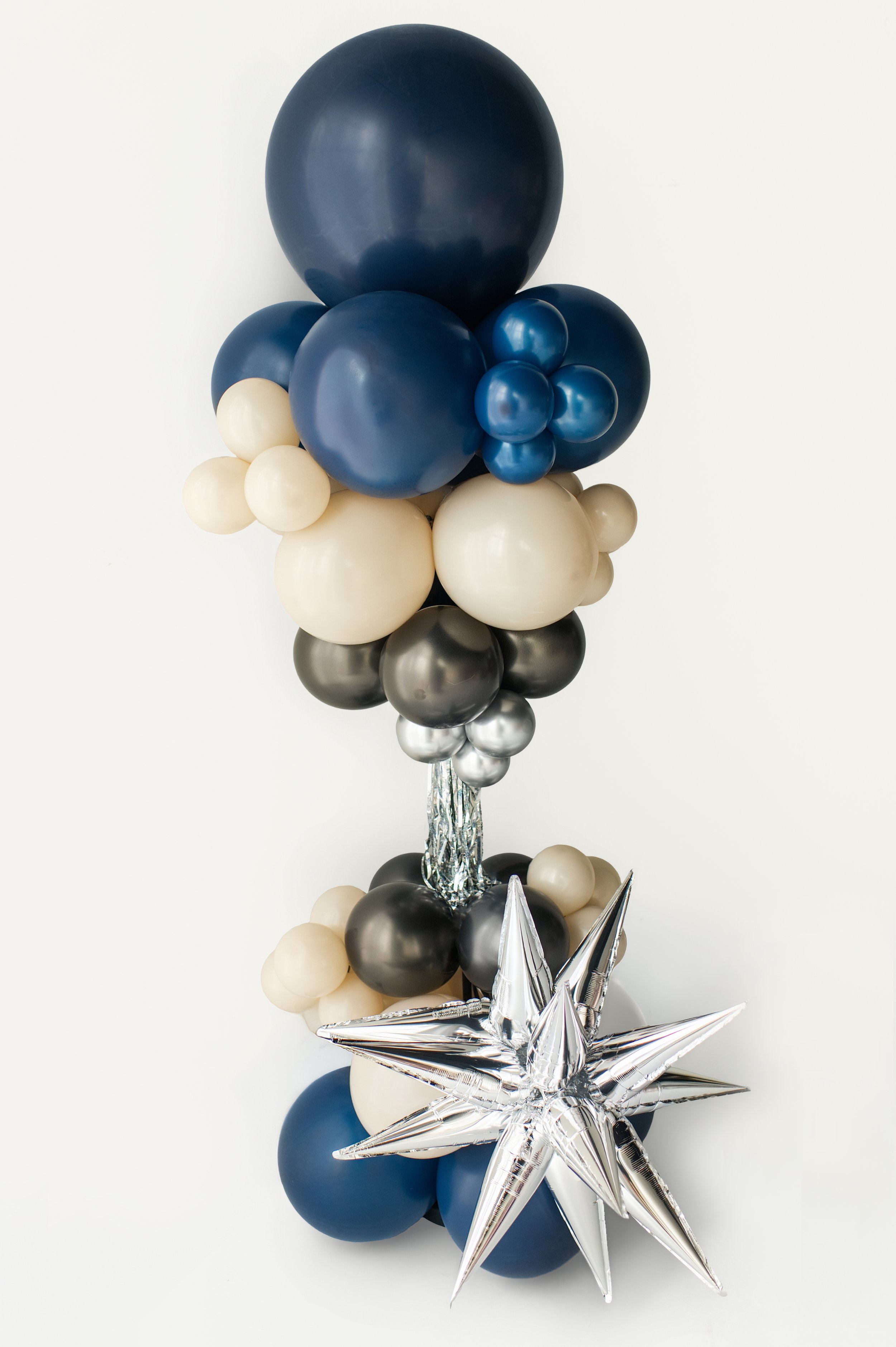 Balloon bouquet with large navy and black balloons, cream and medium blue balloons, and silver star-shaped balloons, arranged on a white background with a helium-filled base.