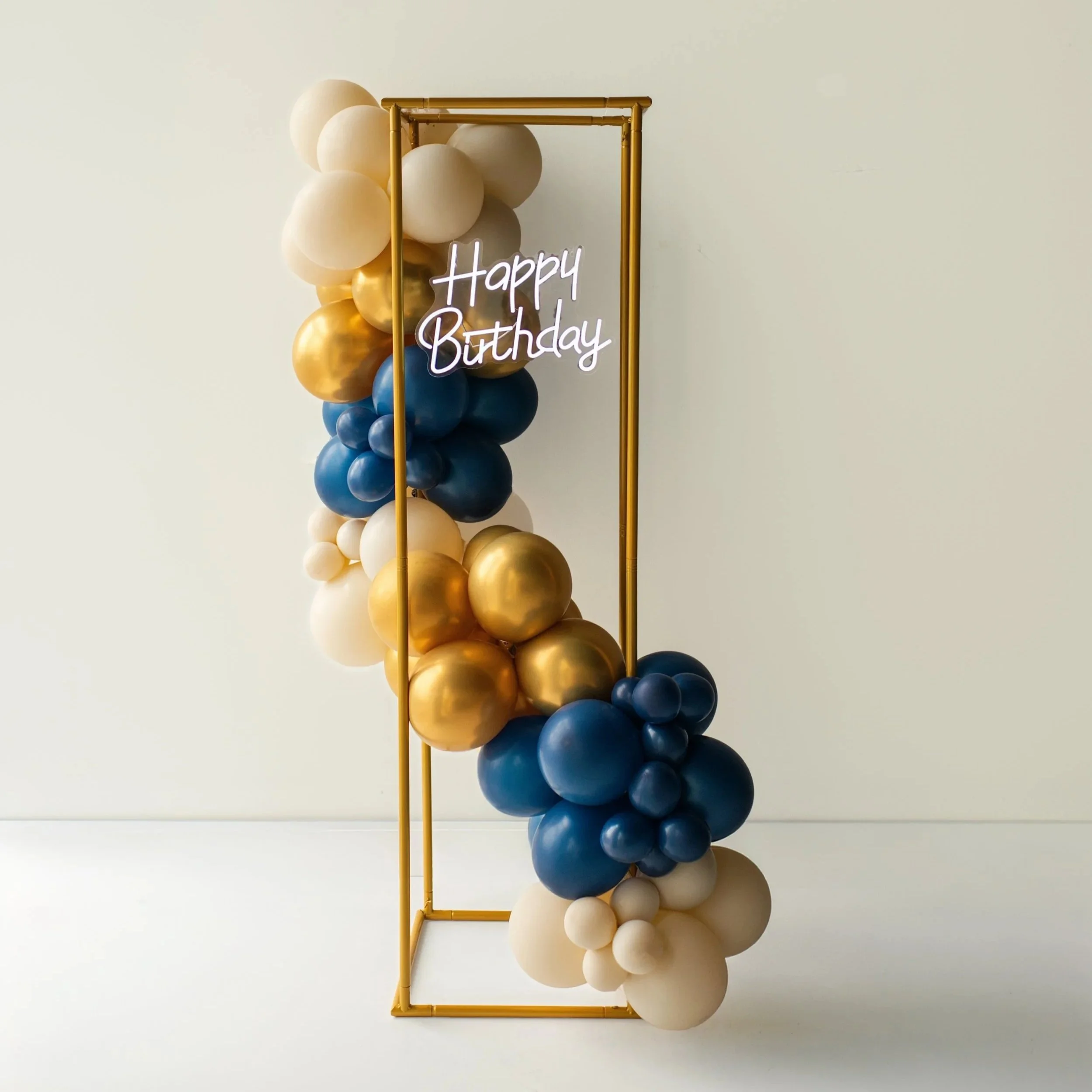 Colorful balloon arrangement with a neon sign that reads 'Happy Birthday' and a gold geometric frame.
