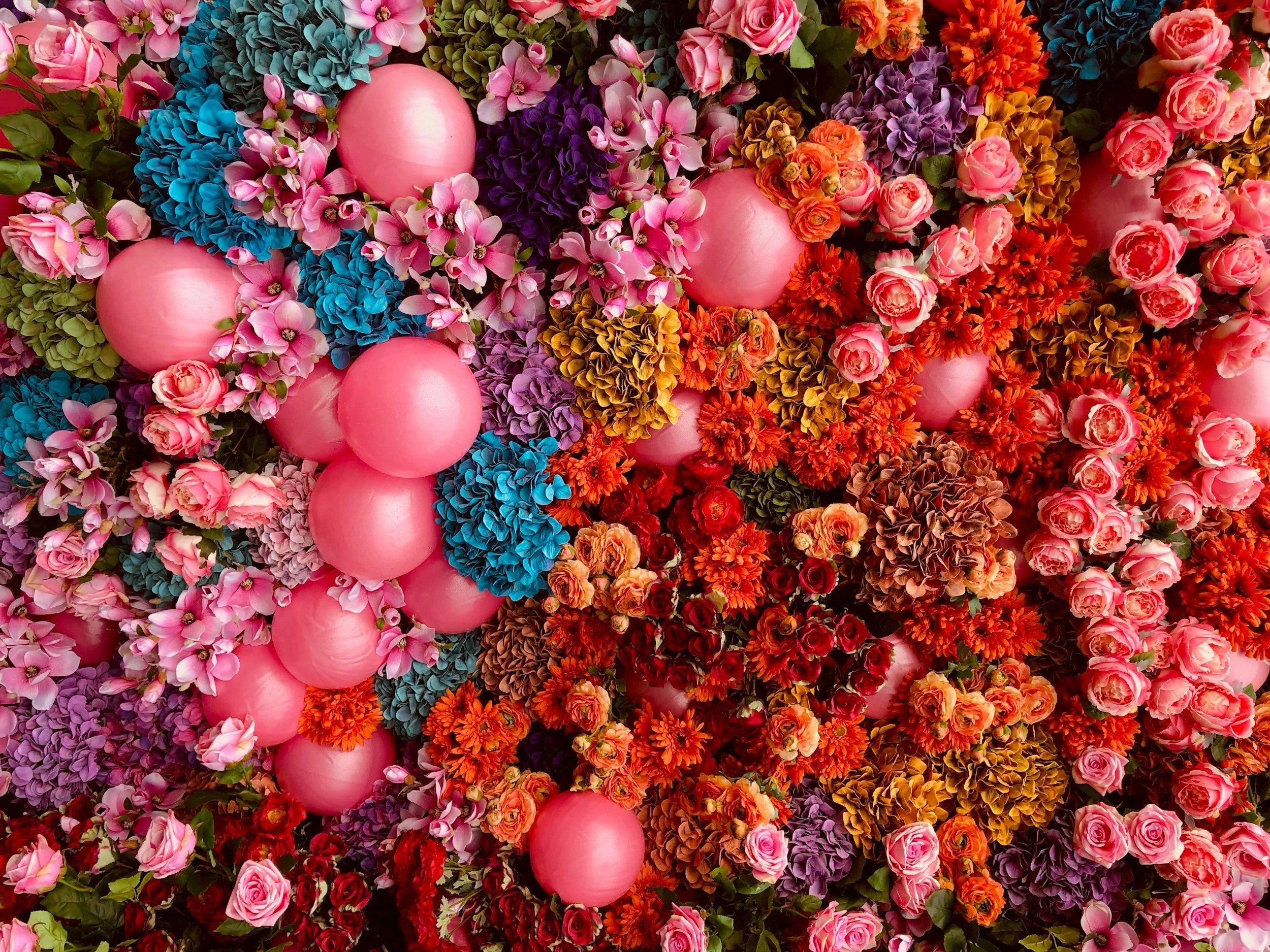 A colorful arrangement of various flowers including pink roses, purple hydrangeas, orange marigolds, red roses, and pink balloons.