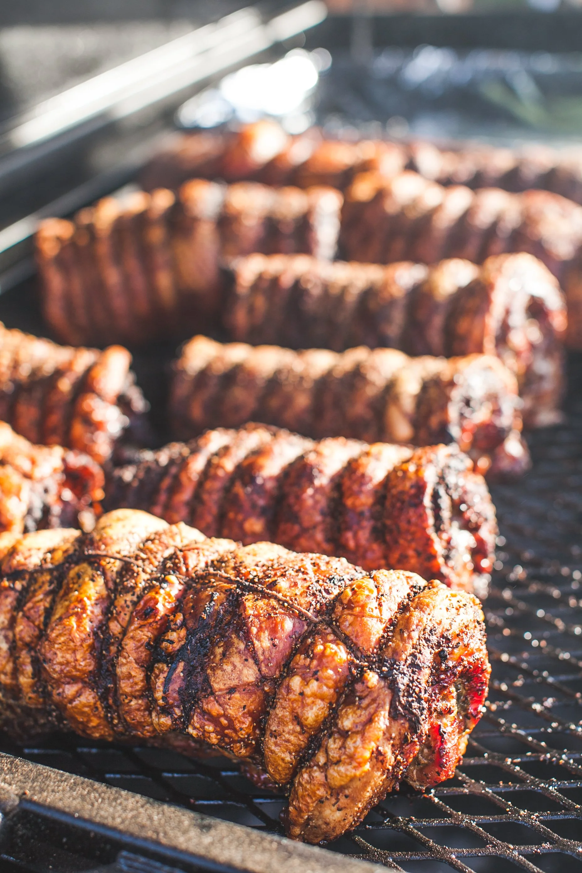 Close-up of seasoned and coated rack of ribs cooking on a grill with grill grates visible underneath.
