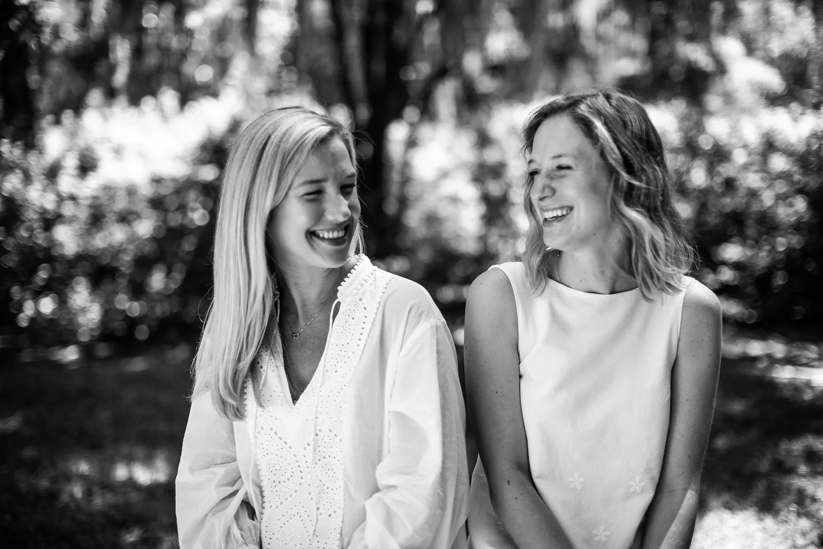 Two women in white dresses laughing together in black and white