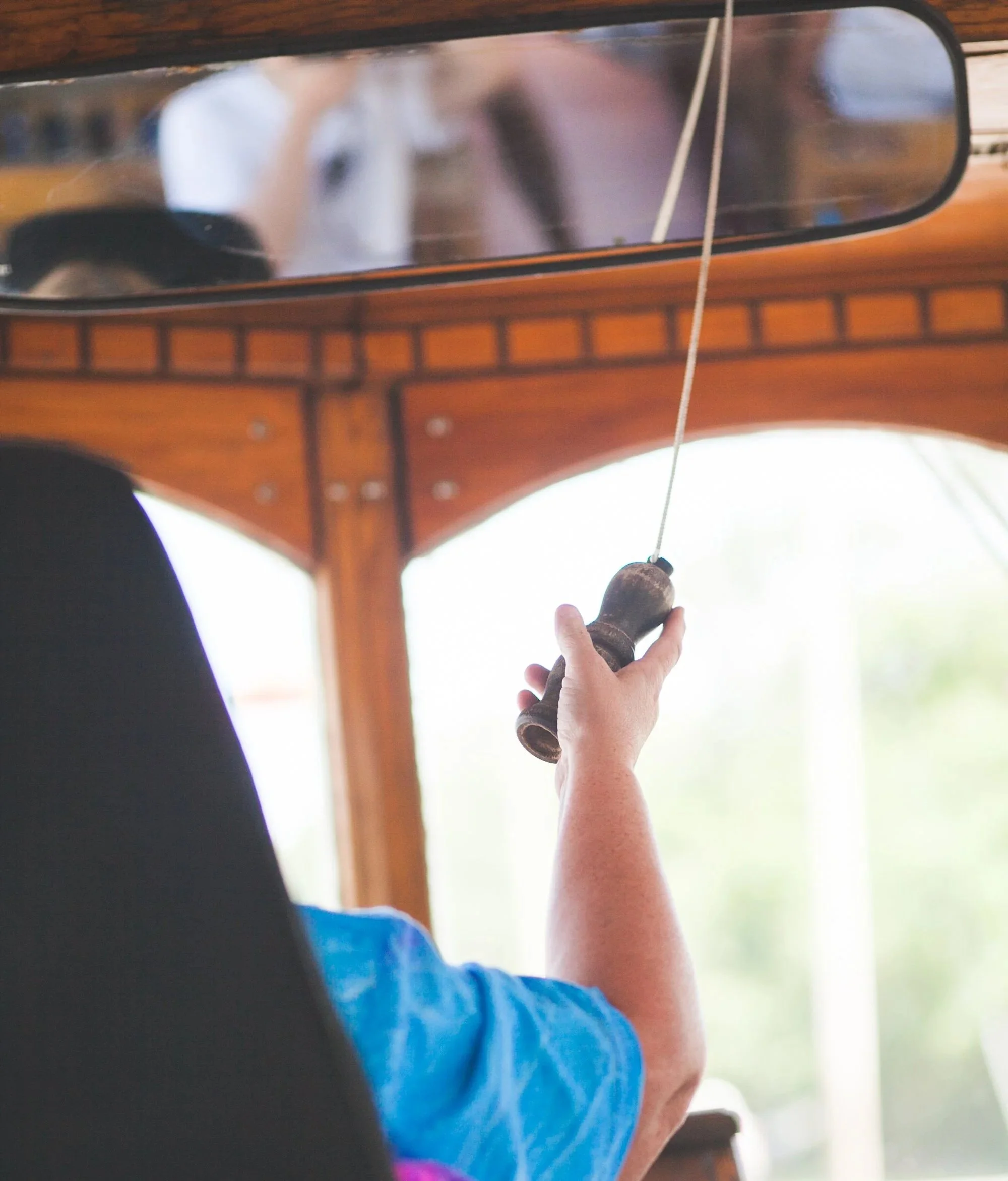 A person's hand holds a wooden handle attached to a fishing rod with a fishing line.