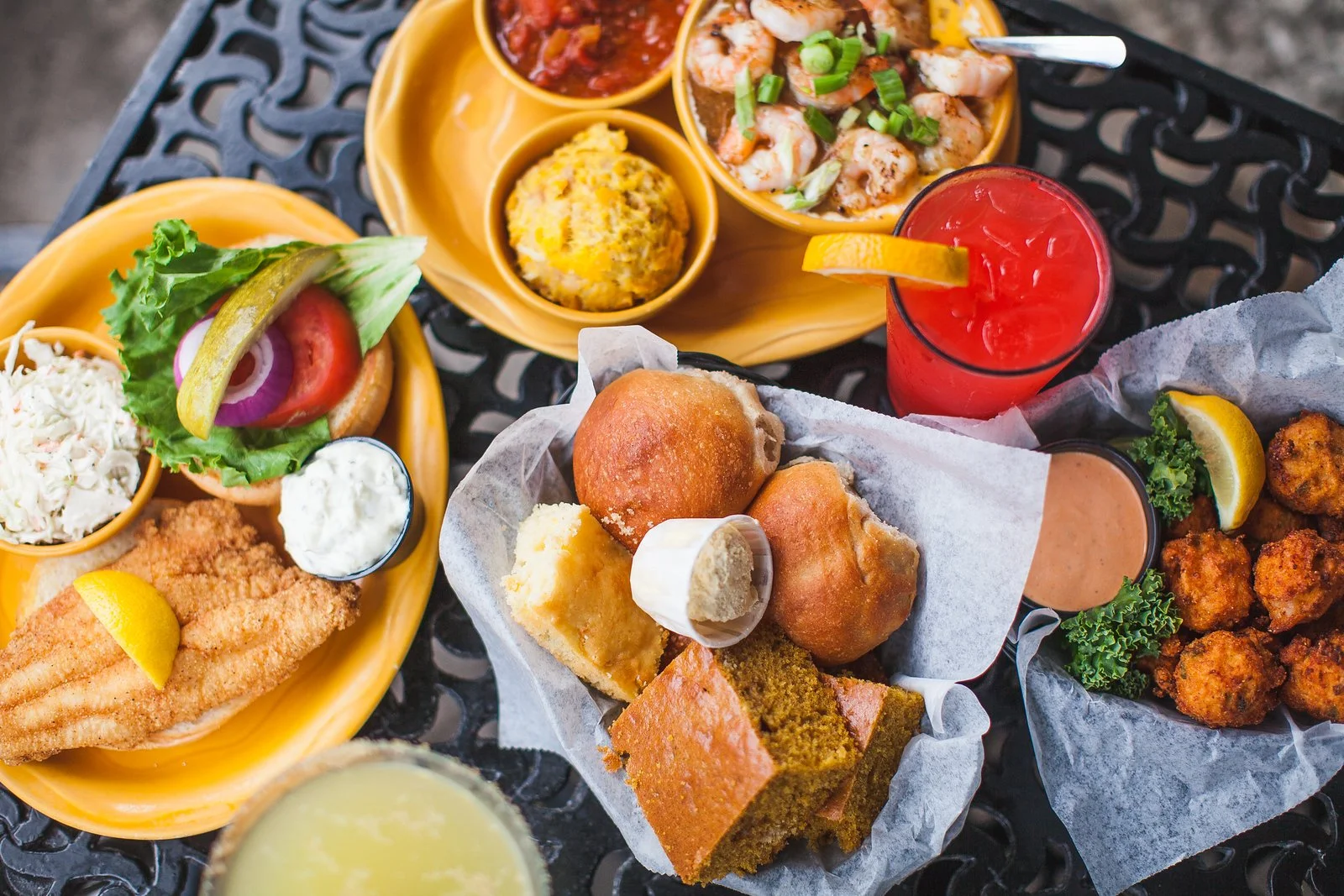 Assorted fried foods, seafood, salads, bread, and drinks on a black outdoor table.
