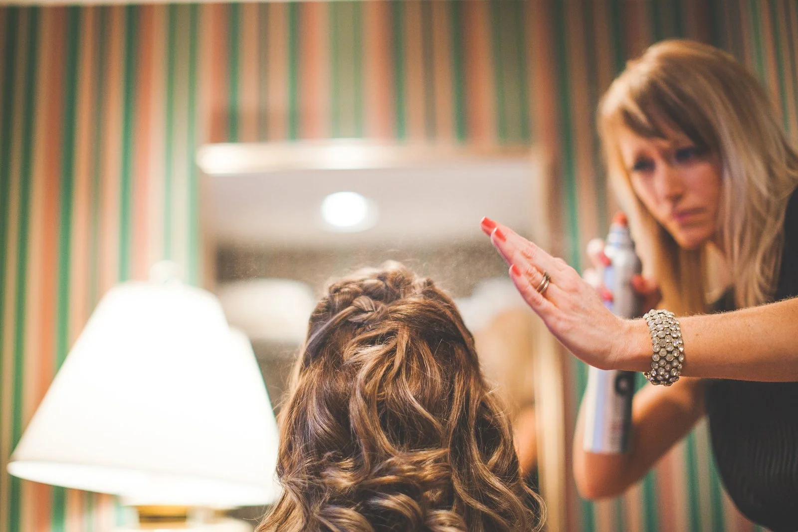 Stylist spraying hairspray on an updo in a hotel room