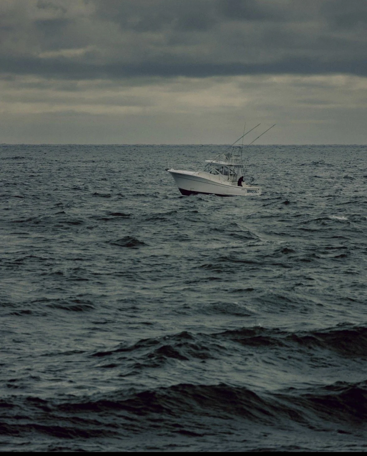 A small white boat on choppy ocean waves under cloudy sky.