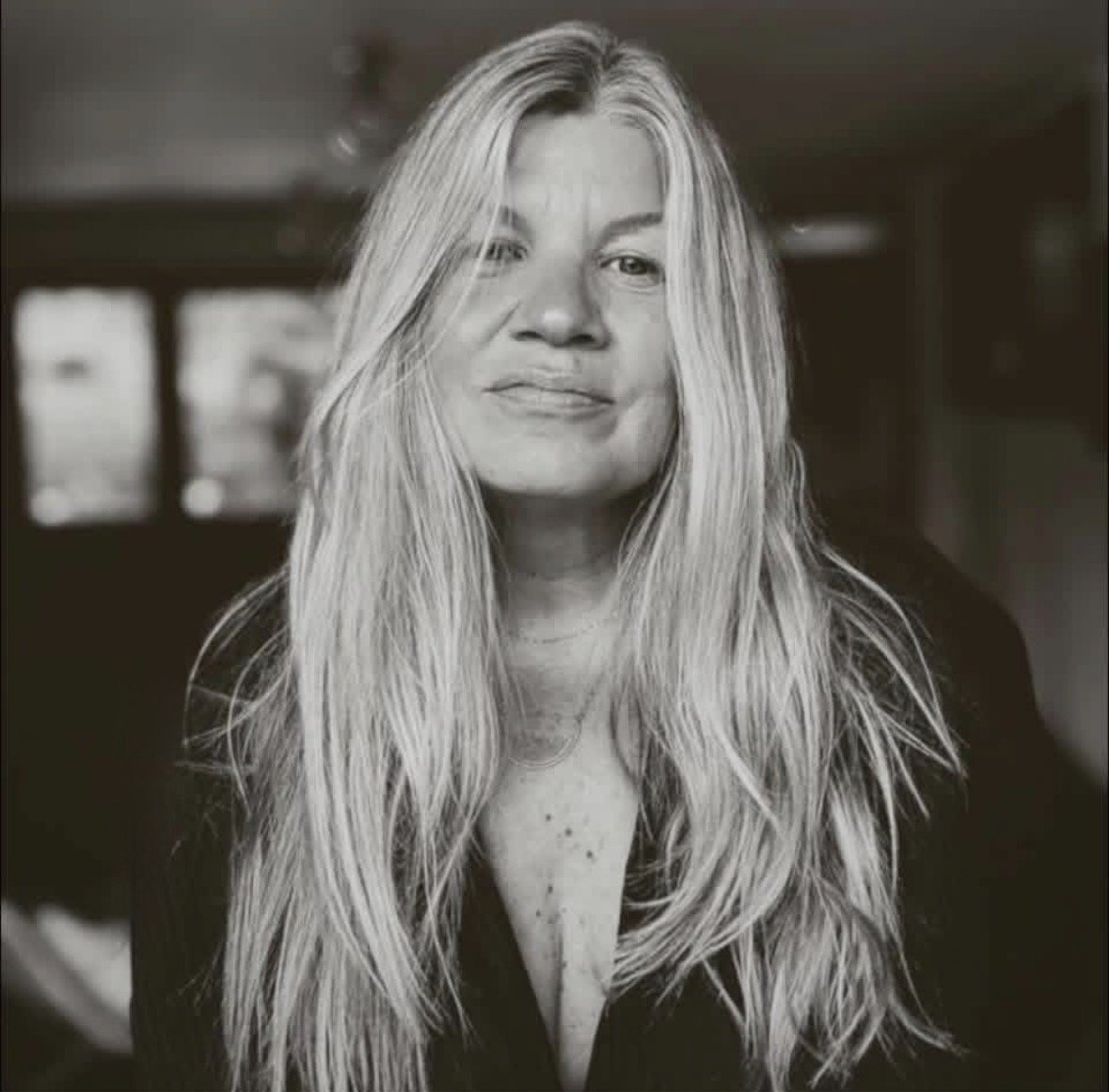 Black and white portrait of a woman with long, blonde hair and a slight smile, sitting indoors.