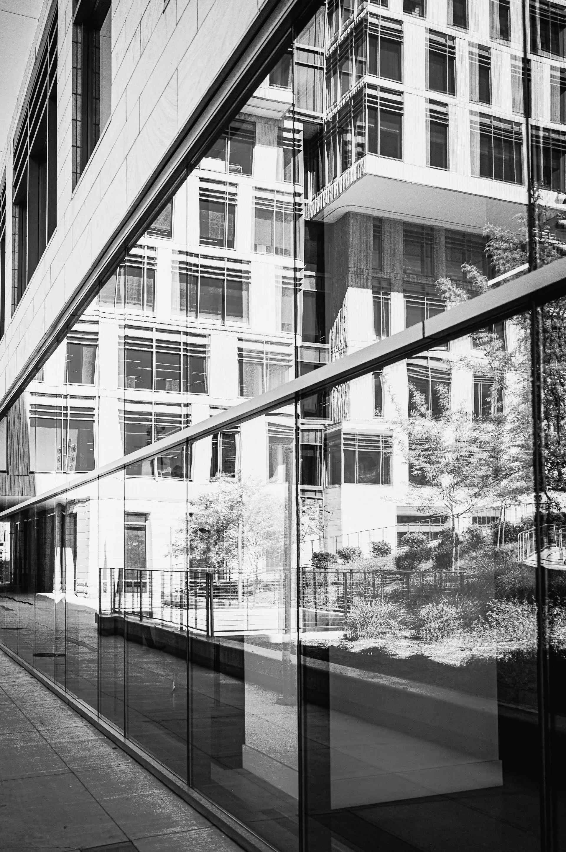 Black and white photo of modern building reflected in glass window, showing geometric patterns and architectural details.