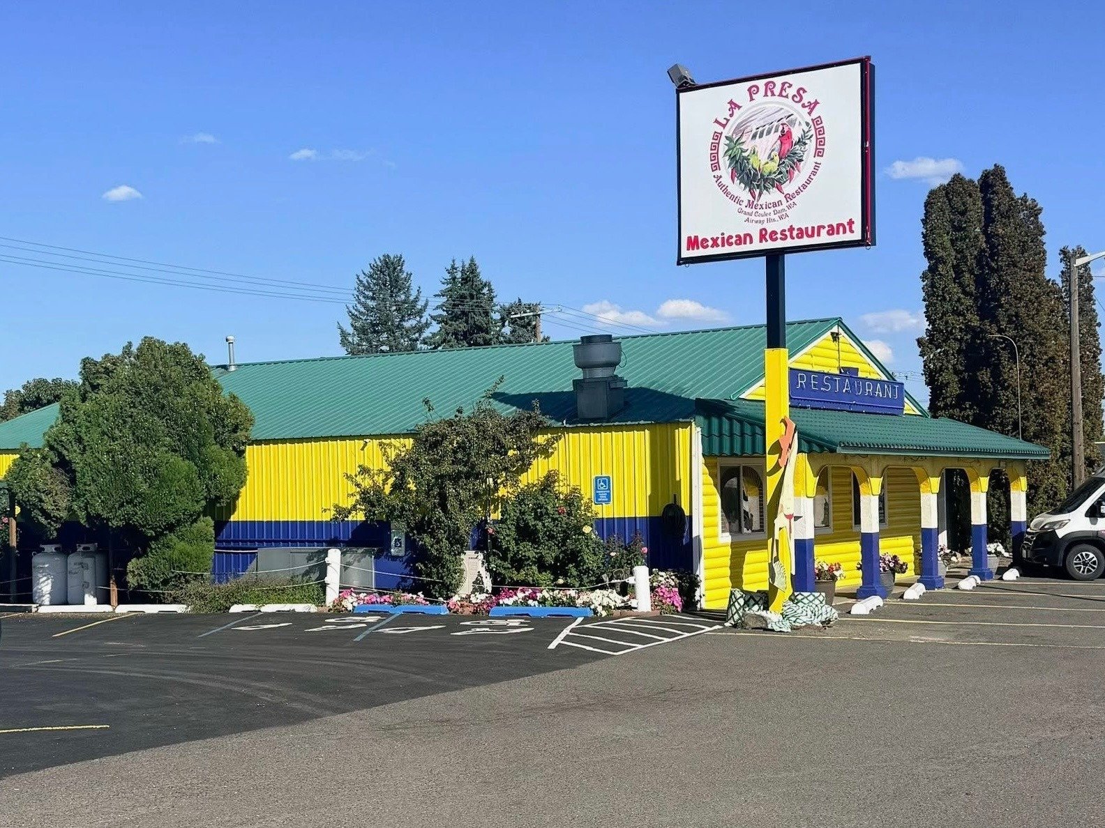 Colorful Mexican restaurant building with yellow, blue, and green exterior, with parking lot in front and bright blue sky above.
