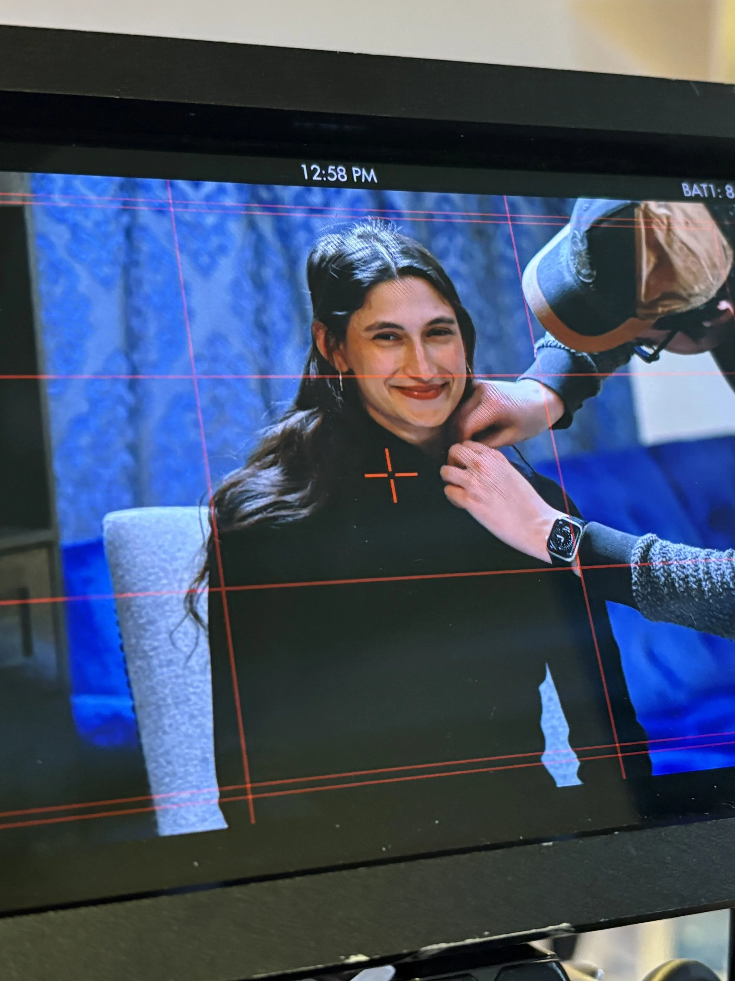 Monitor screen displaying a woman with dark hair, smiling, with a blue textured background, and a person adjusting her hair or face.