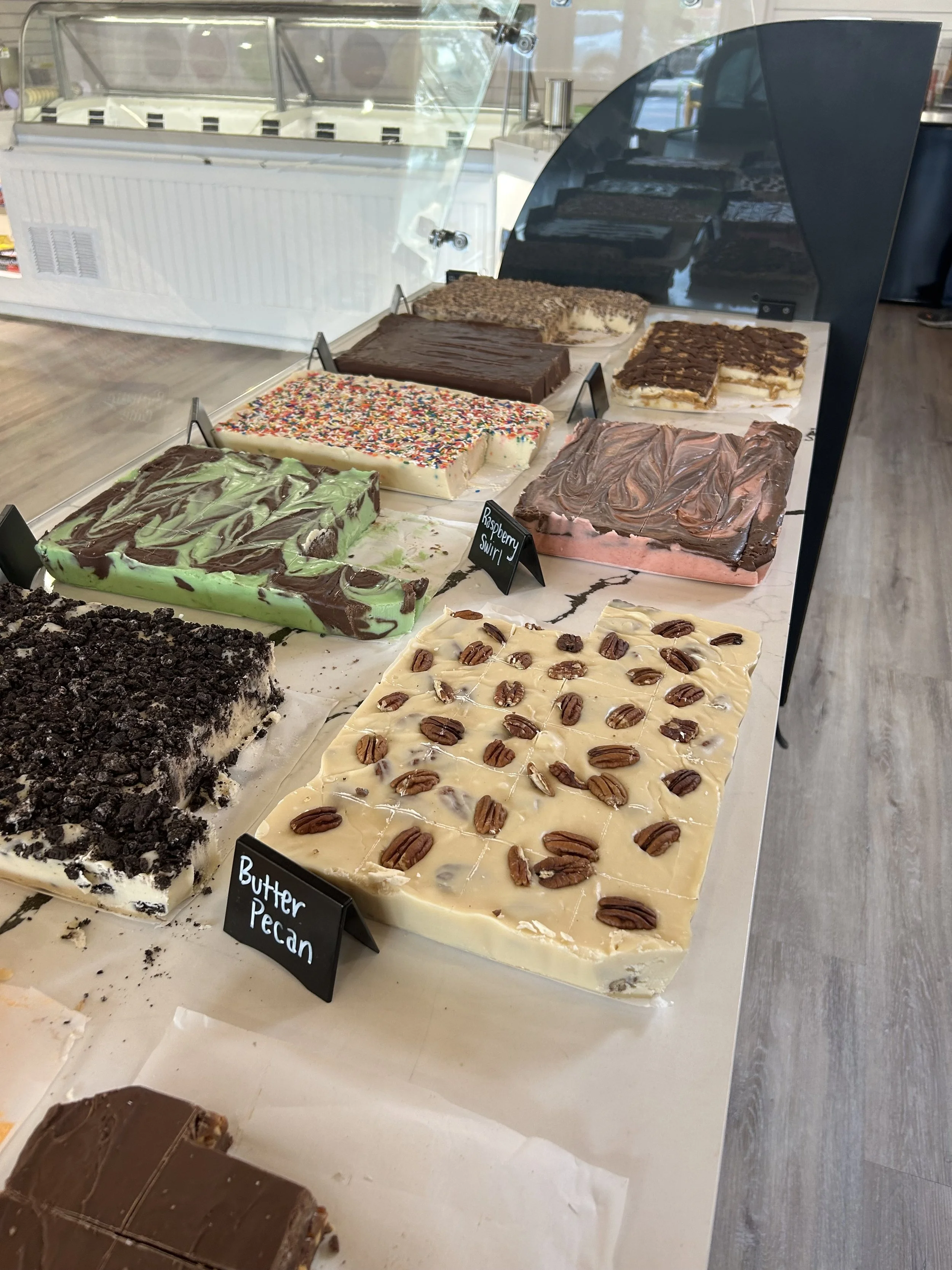 Various types of fudge displayed in a glass case with some labeled, such as 'Butter Pecan' and 'Raspberry Swirl.'