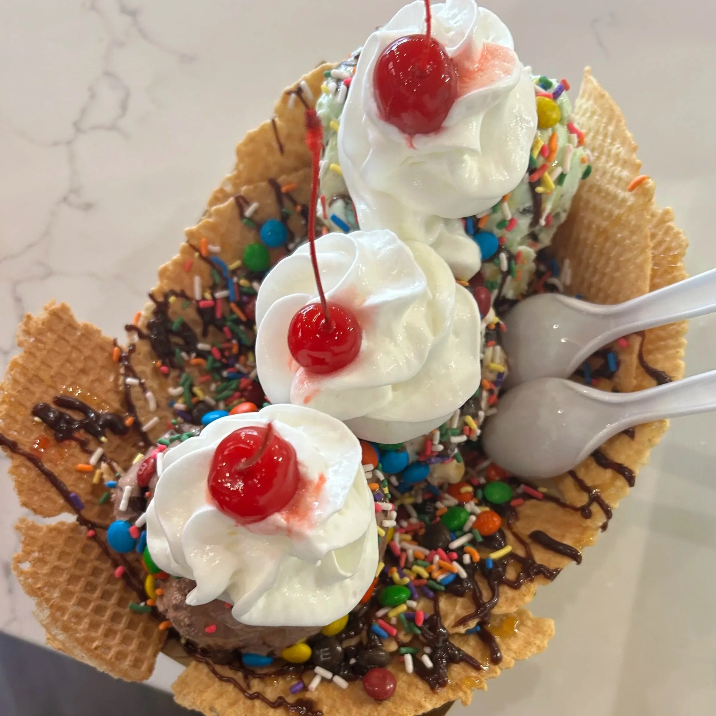 Ice cream nachos topped with whipped cream, maraschino cherry, multicolored sprinkles, chocolate syrup, and crunchy cookie pieces.