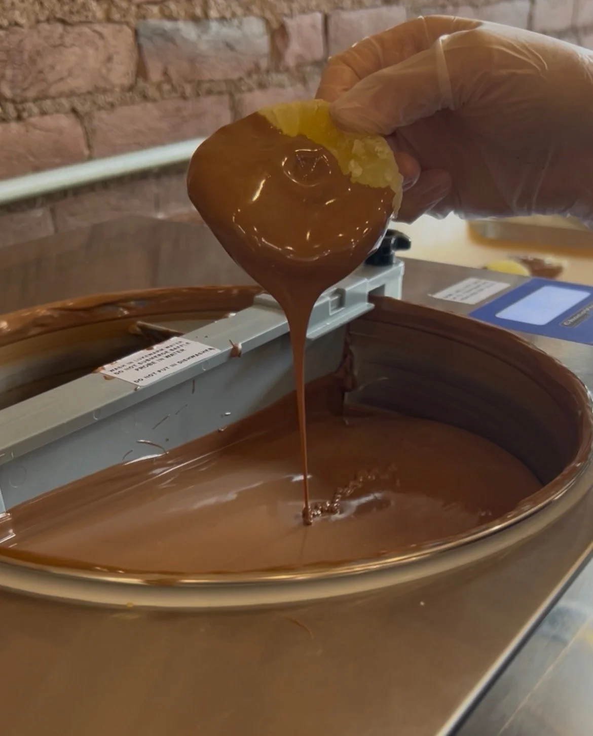 Close-up of someone dipping candied pineapple into chocolate.