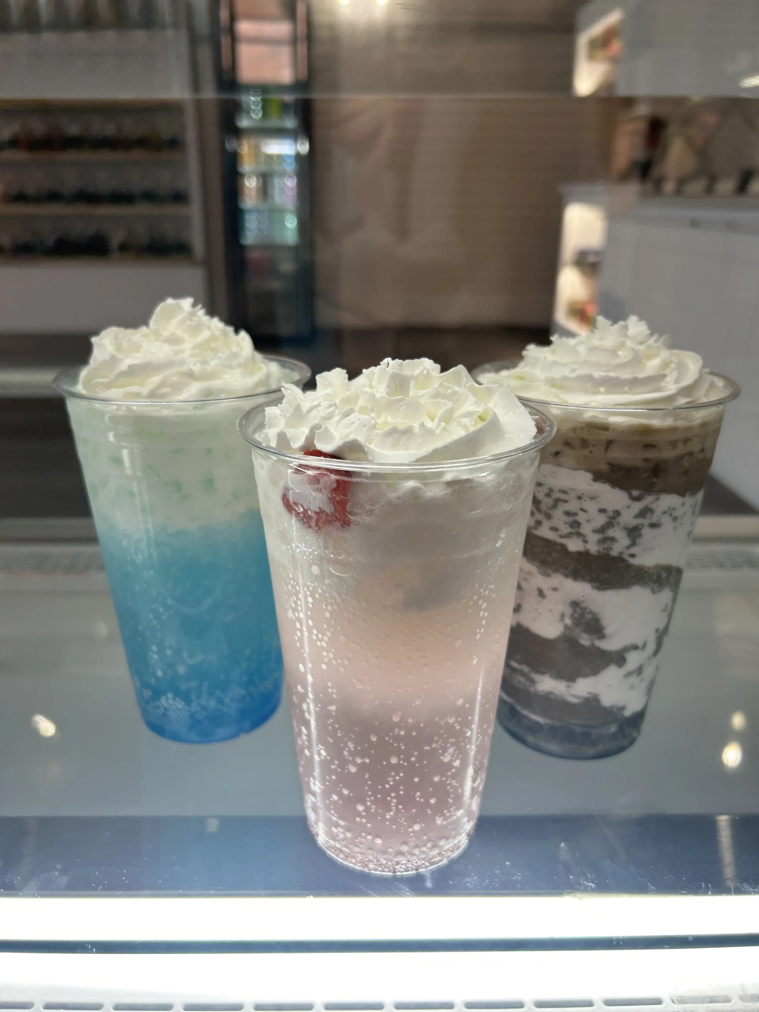 Three dirty soda flavors  with whipped cream on top. The left one is blue Raspeberry and coconut, the middle is strawberry and vanilla and the last is toasted marshmallow