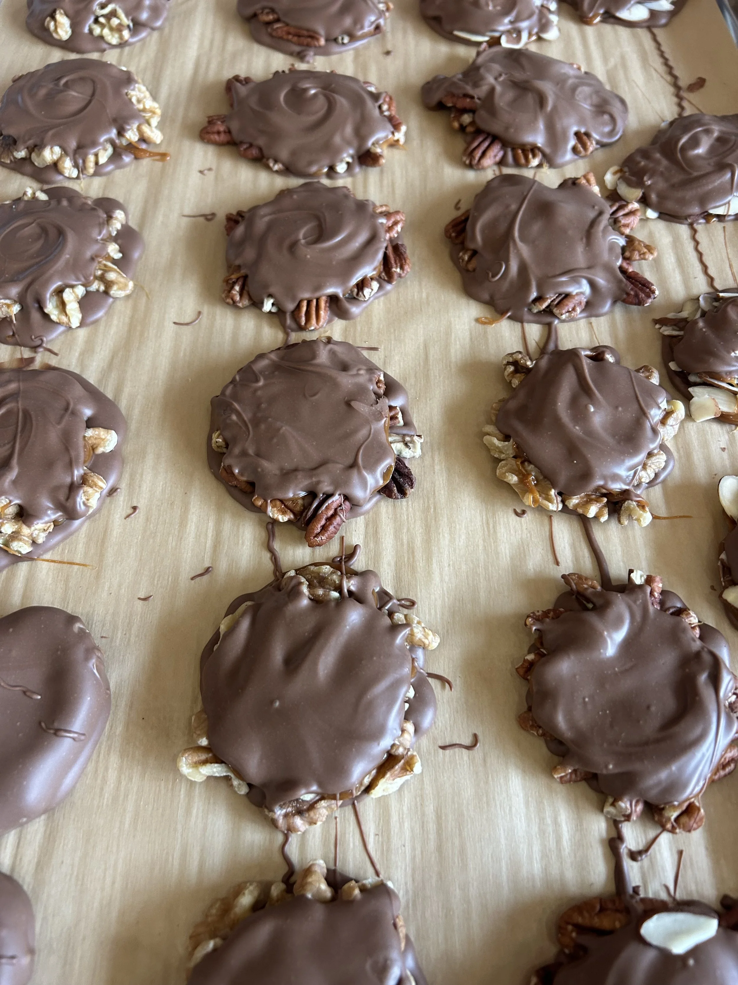 Chocolate-covered treats with nuts on top, arranged on a wooden surface.