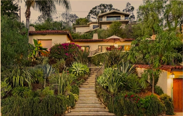 A hillside property with multi-level modern houses and lush landscaped garden with stairway path.