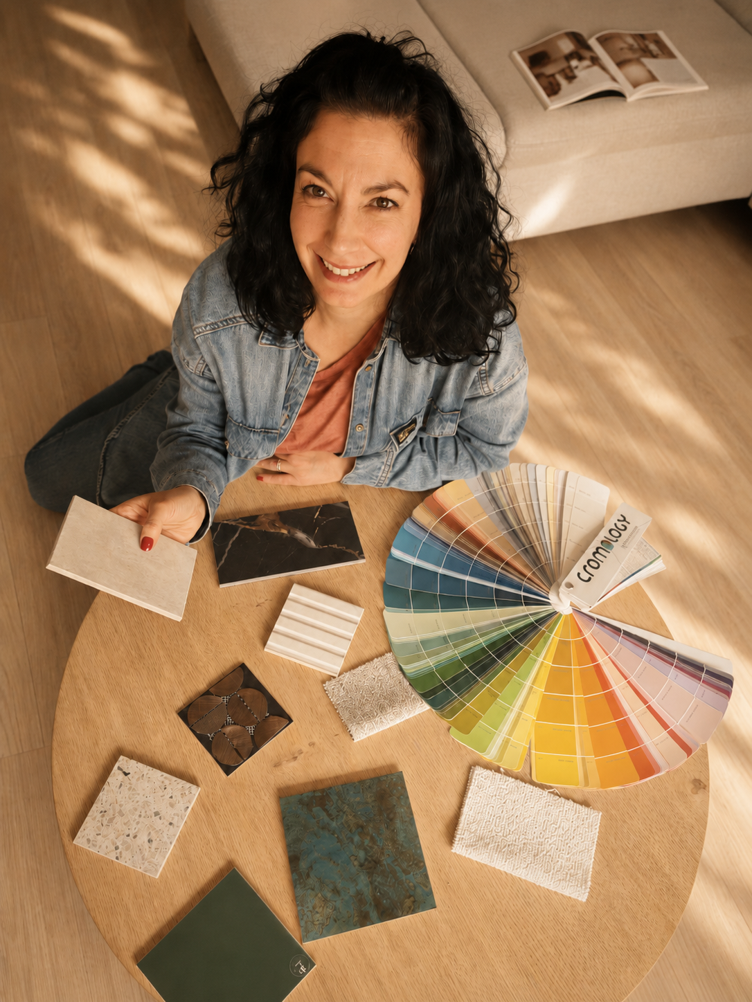 Femme souriante regardant la caméra, assise à une table avec une sélection d'échantillons et de palettes de couleurs pour la décoration intérieure.