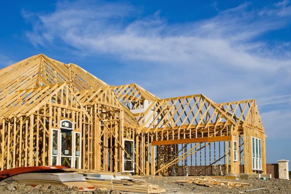 Wooden framing of a house under construction with a blue sky and clouds in the background.