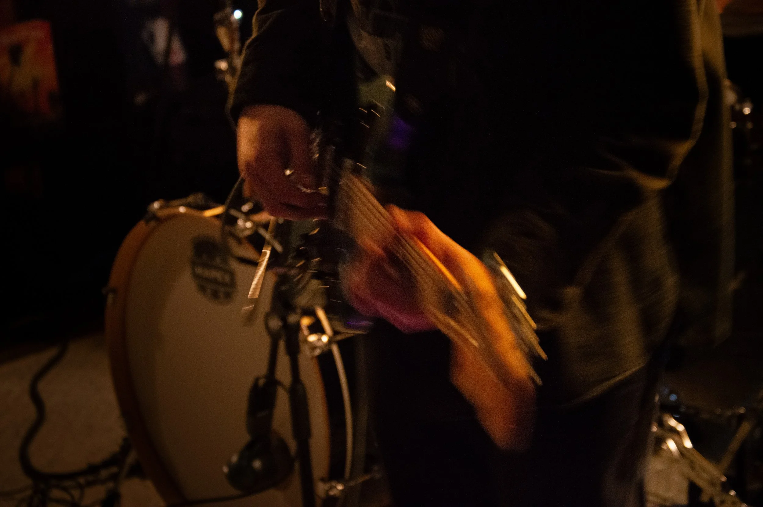 A person playing an acoustic guitar. The image is blurry and taken in a dimly lit environment.