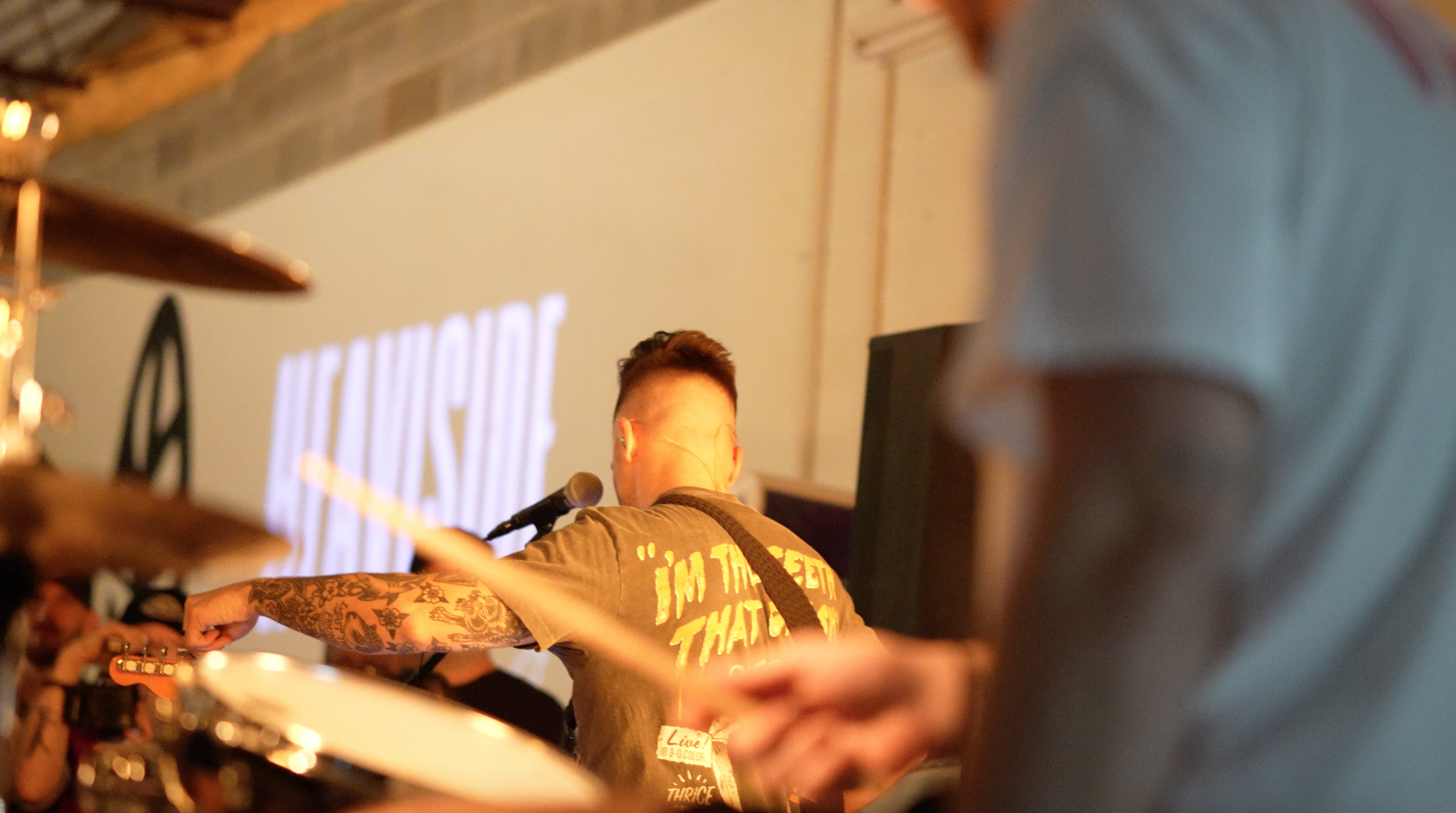 A person with tattoos on their arm playing music at an indoor event, with a microphone in front of them and a large screen in the background displaying the words 'Mega Juice'.