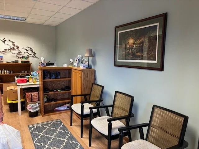 Chiropractic clinic patient waiting area with seating, storage, artwork, and warm wood finishes.