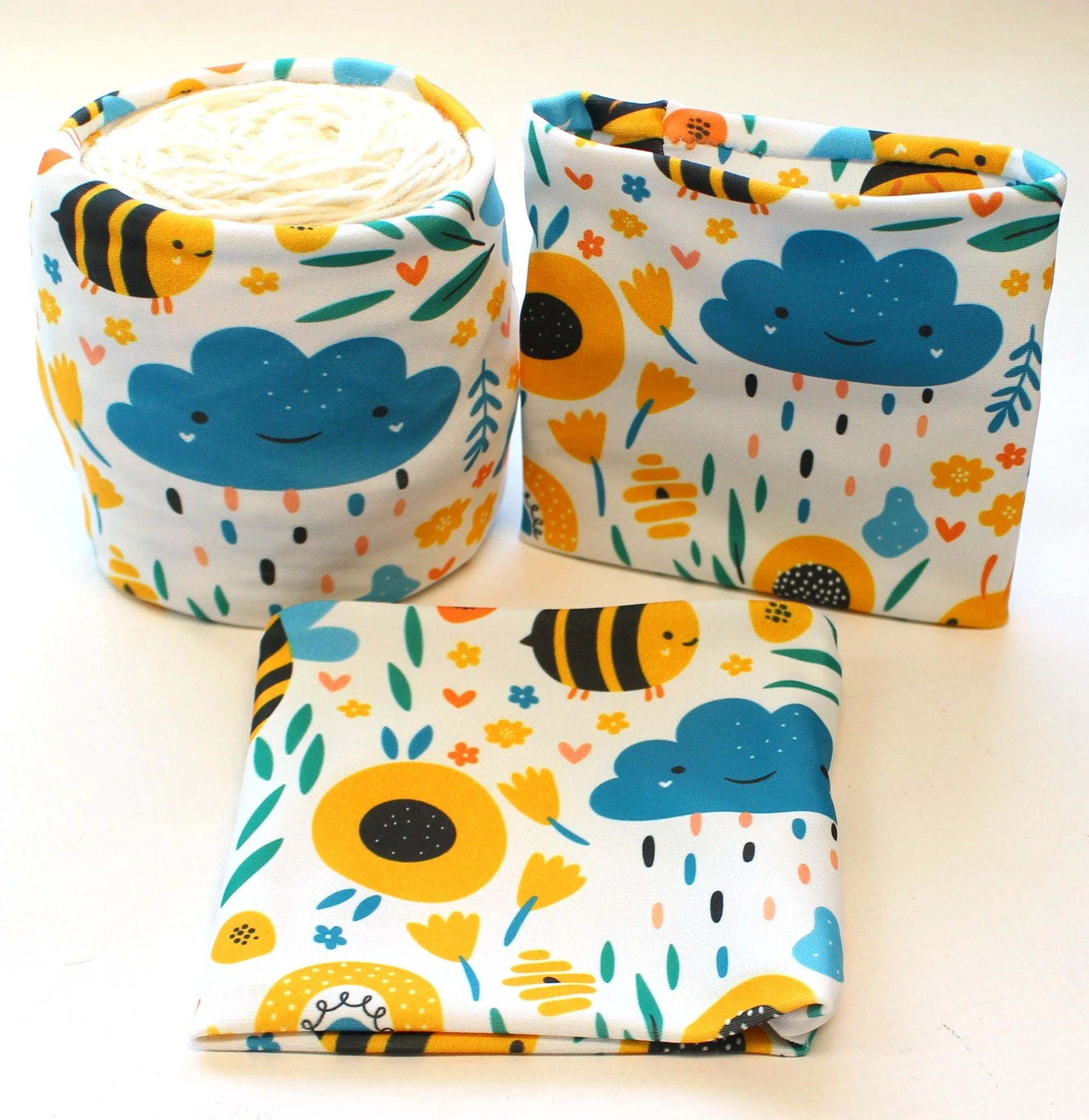 Colorful fabric storage containers with playful animal and weather cloud patterns, one filled with yarn.