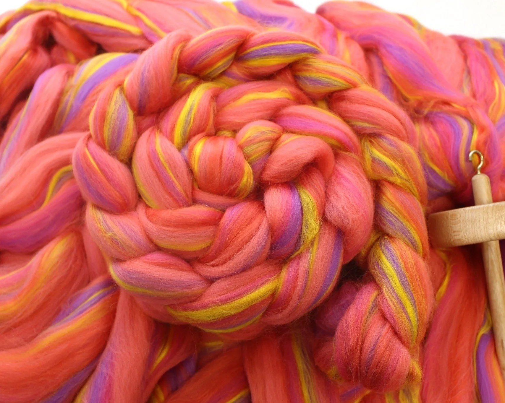 Close-up of multicolored, thick, braided yarn in shades of pink, yellow, and purple with a wooden yarn swift.