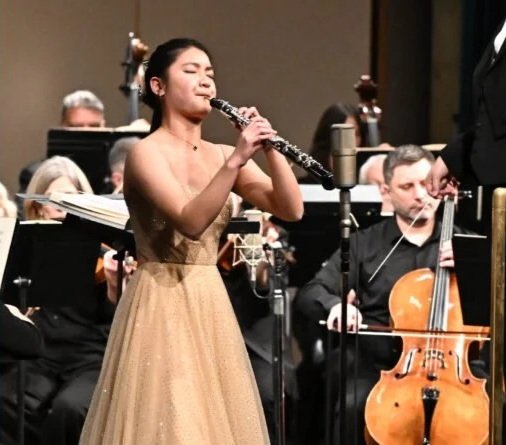 A woman in a gold dress playing the clarinet during an orchestra performance.