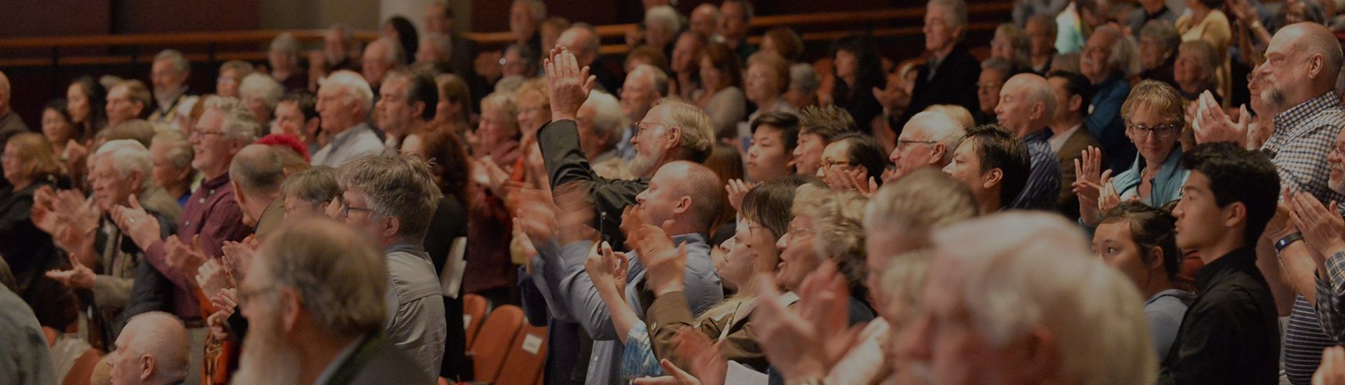 An audience in a theater or auditorium clapping and cheering during a presentation or event.