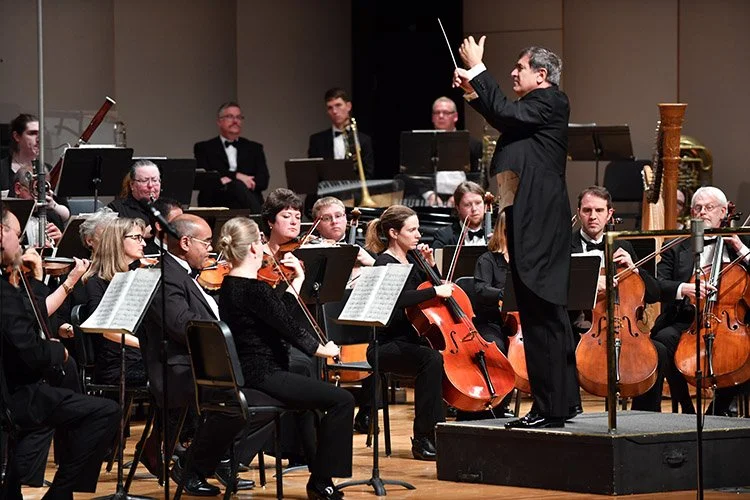 An orchestra performing on stage with a conductor leading them.
