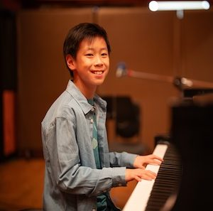 Young boy playing a grand piano in a music studio