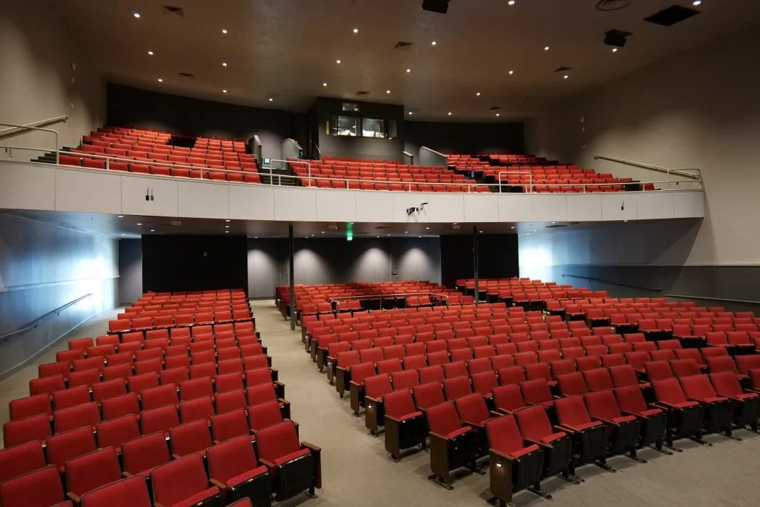 Empty theater auditorium with red seats and multiple levels of seating.