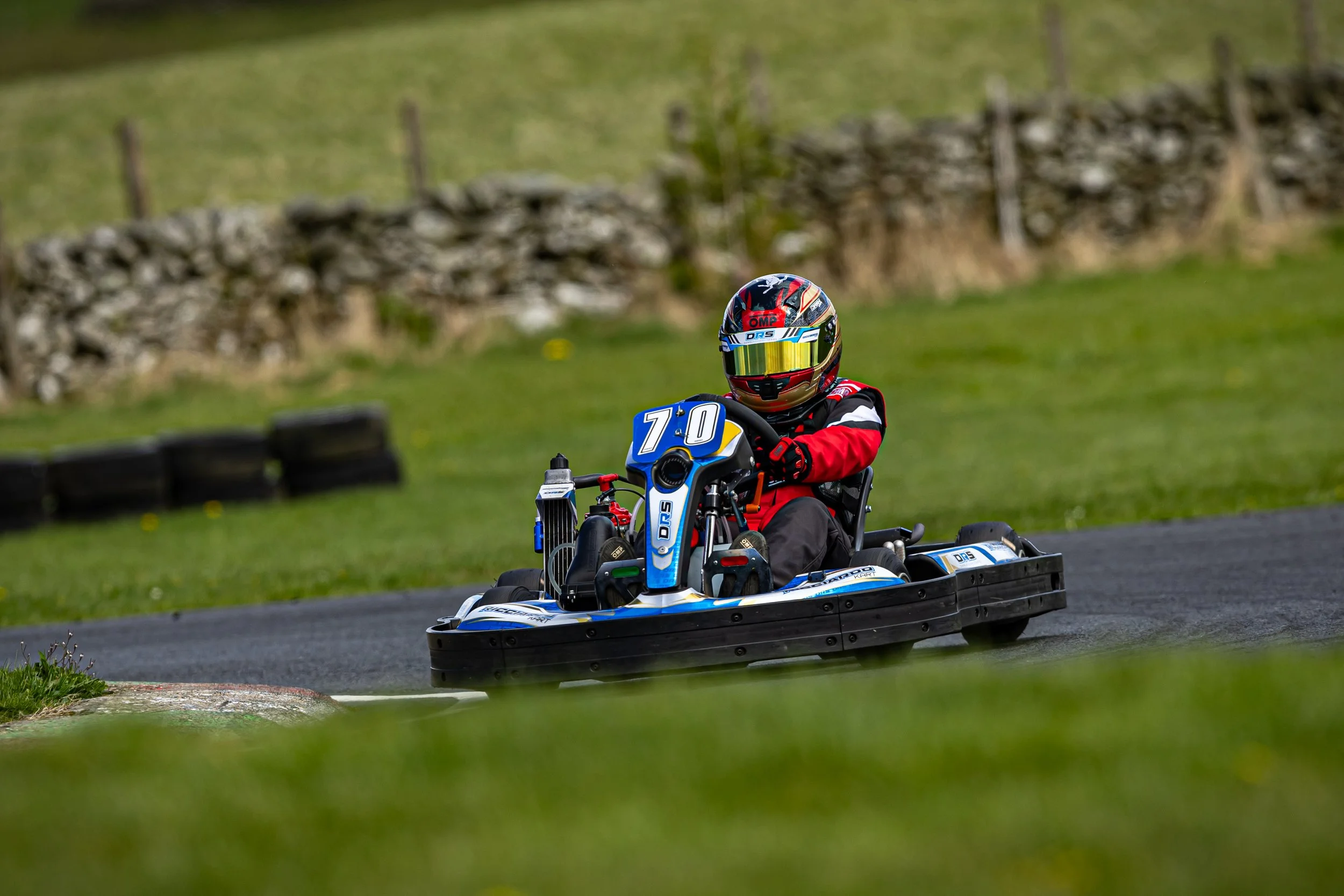 A person in a helmet and racing suit driving a go-kart on a race track.