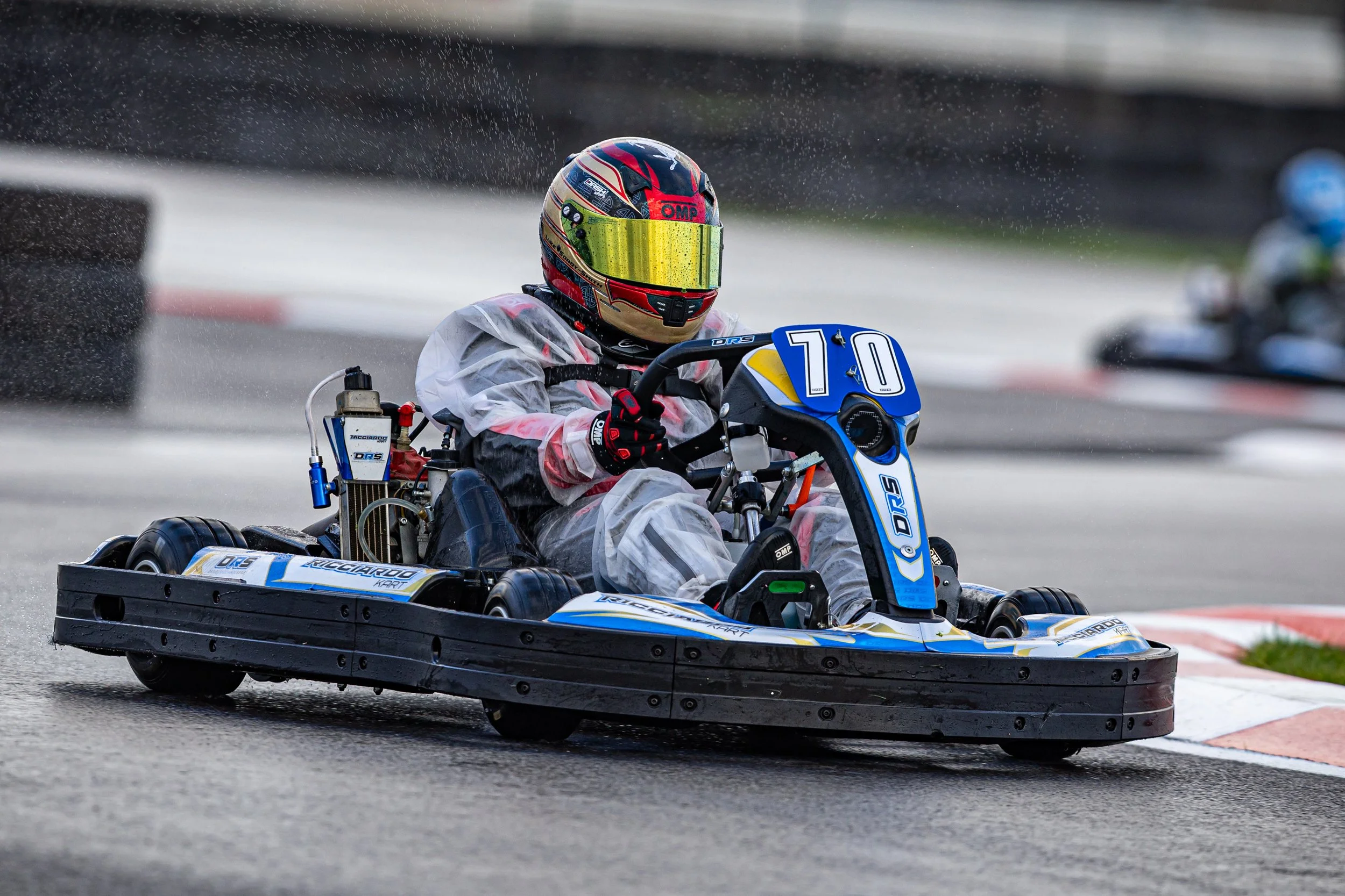A person in a racing helmet and racing gear driving a go-kart on a race track.
