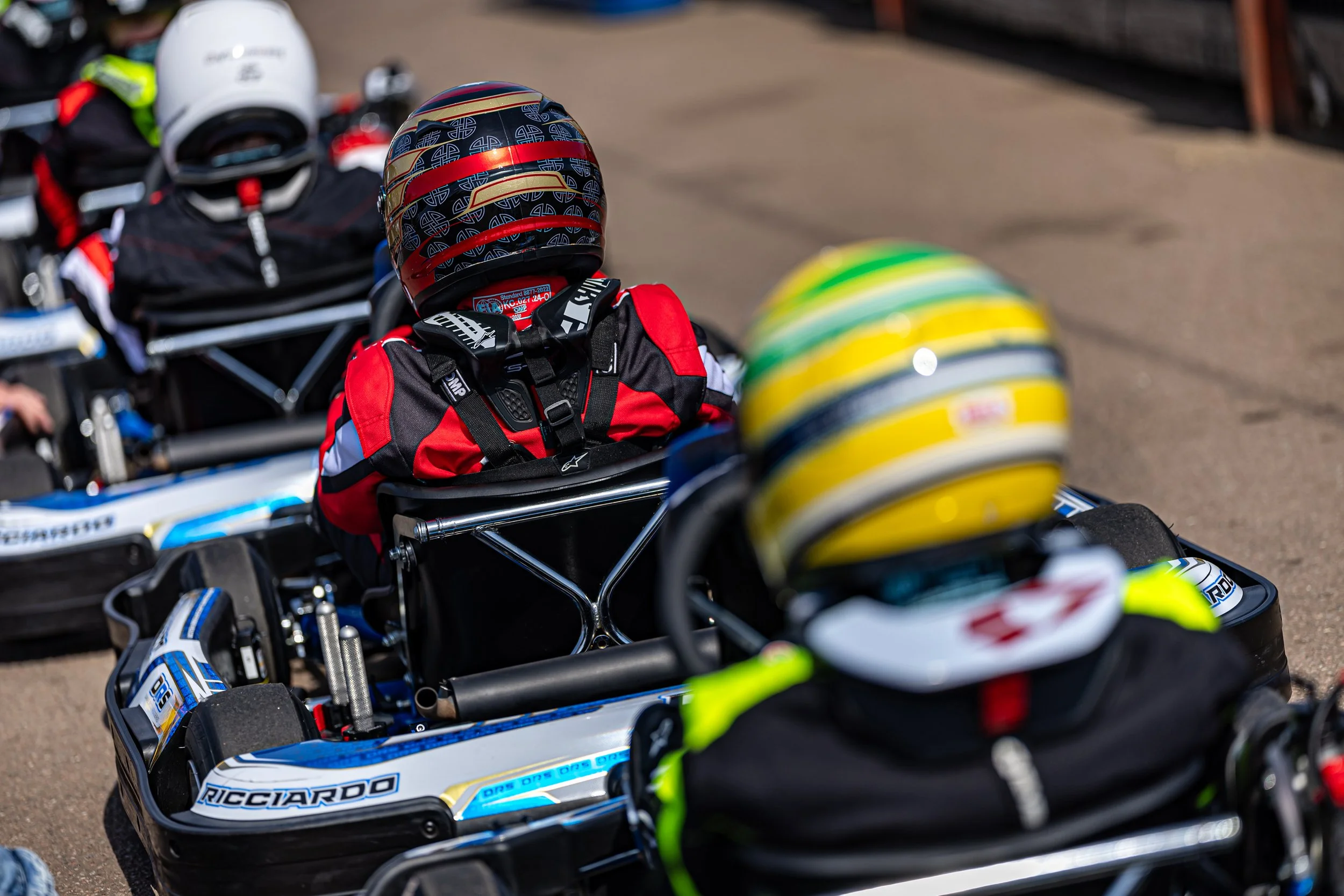 Multiple go-karts lined up with racing helmets on top, ready for a race on an outdoor track.