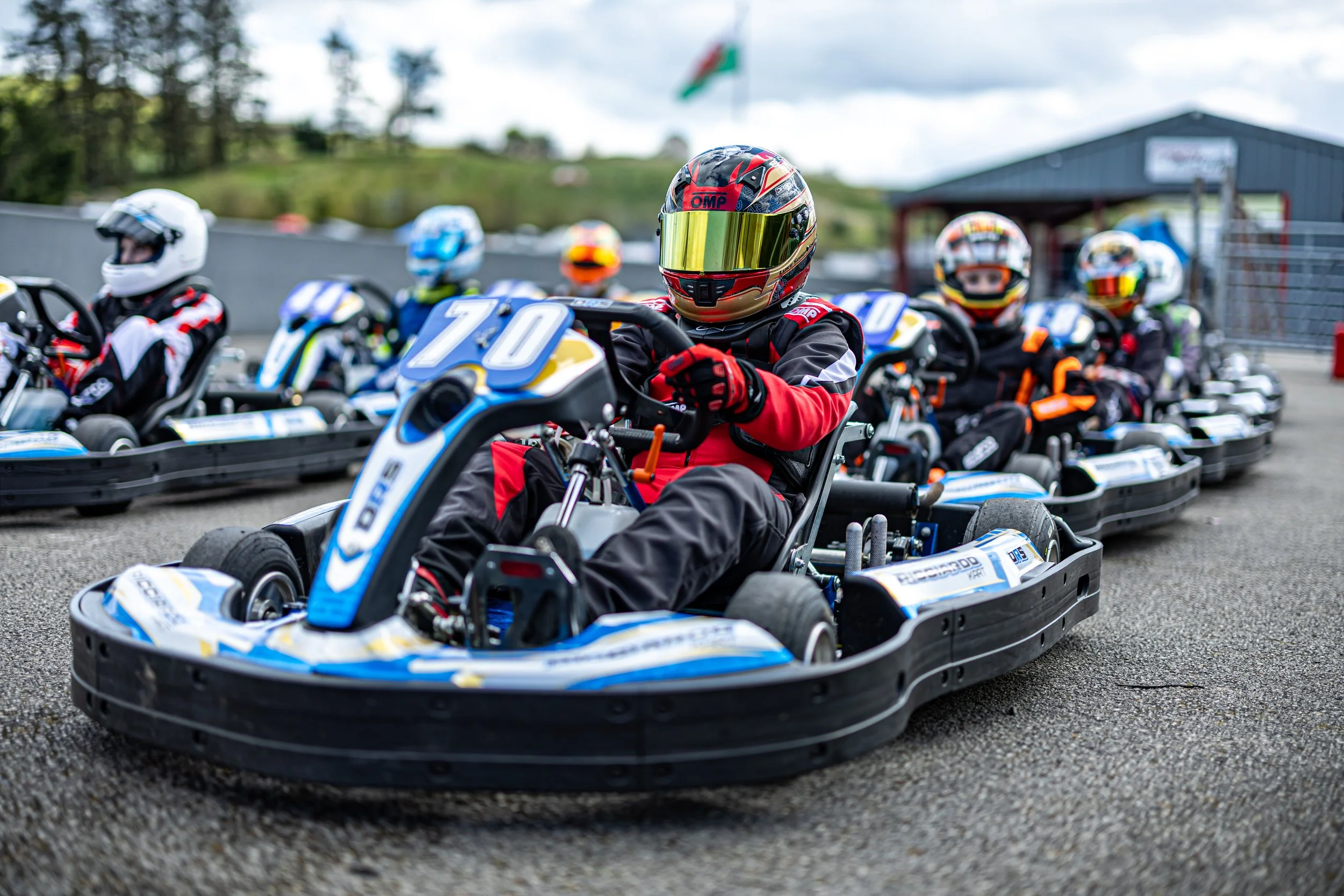 Multiple go-karts lined up on a racetrack with drivers wearing helmets and racing suits, ready for a race.
