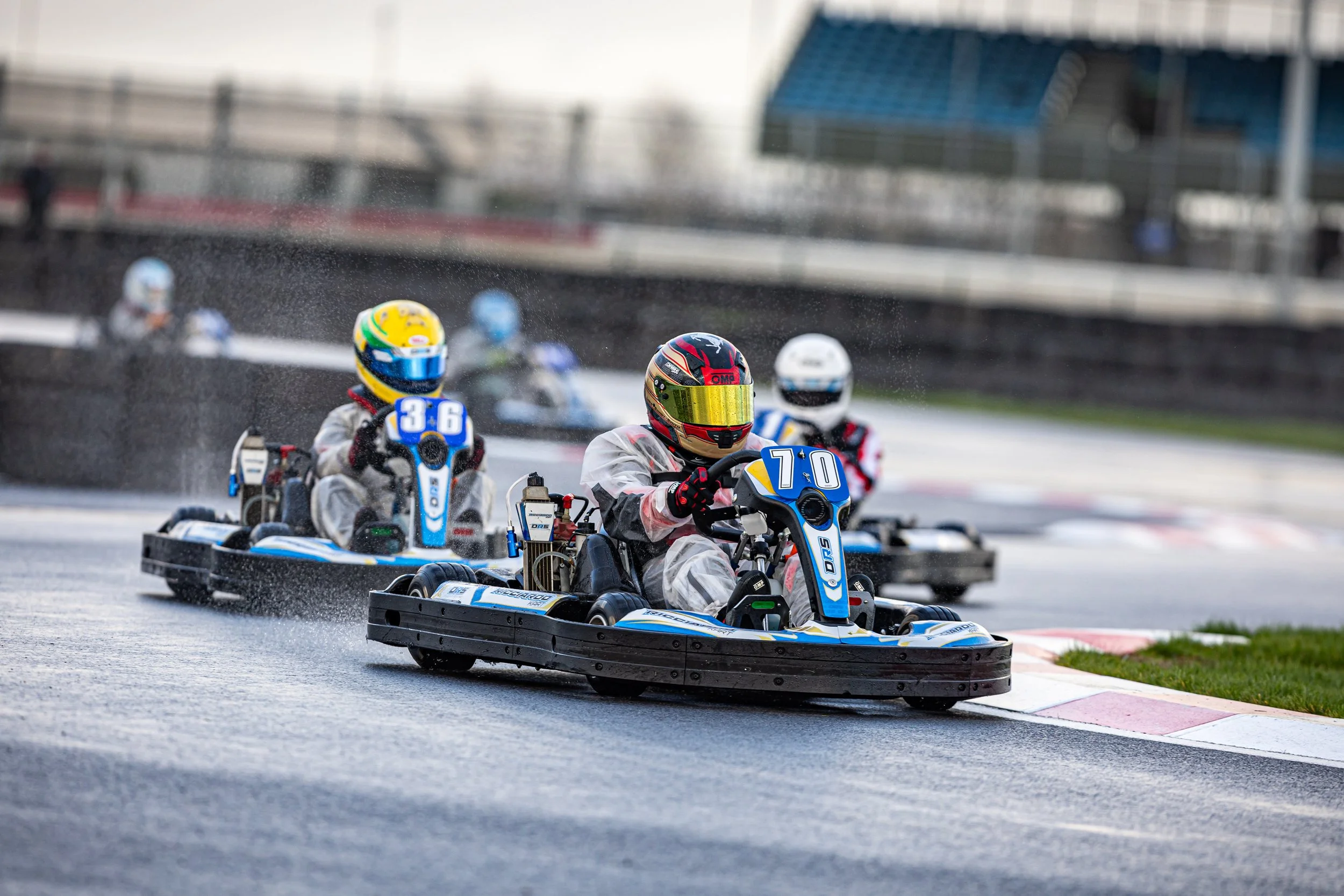 Race car drivers in go-karts racing on wet track at a racing circuit.