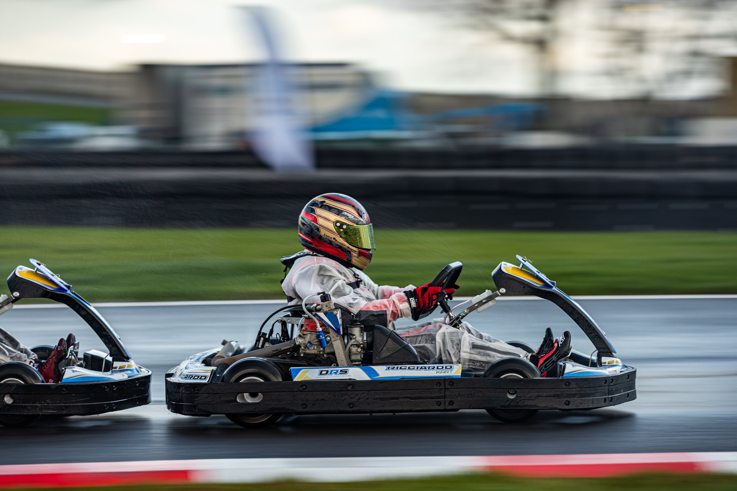 A go-kart racer wearing a helmet and racing suit driving on a track.