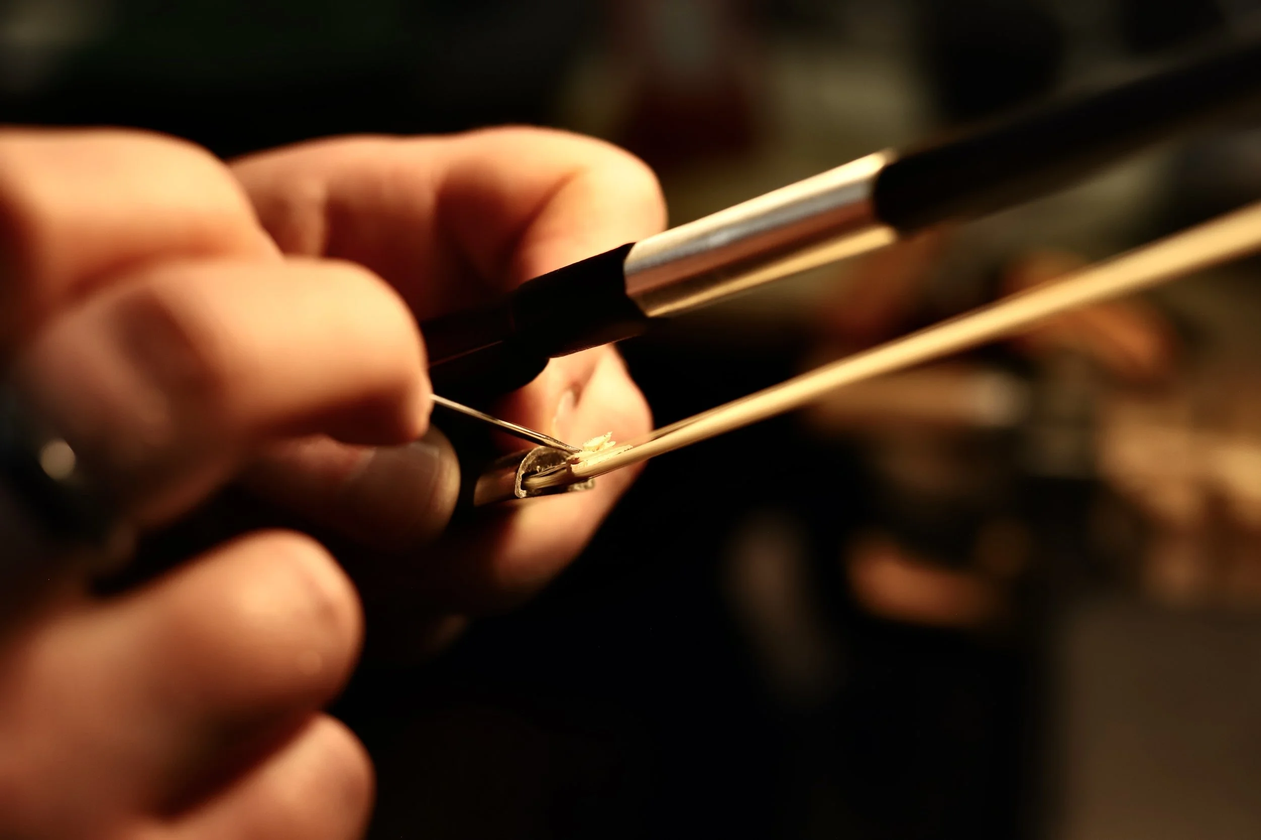 Close-up of a person's hand holding a violin bow and carpentry tools with blurred background.