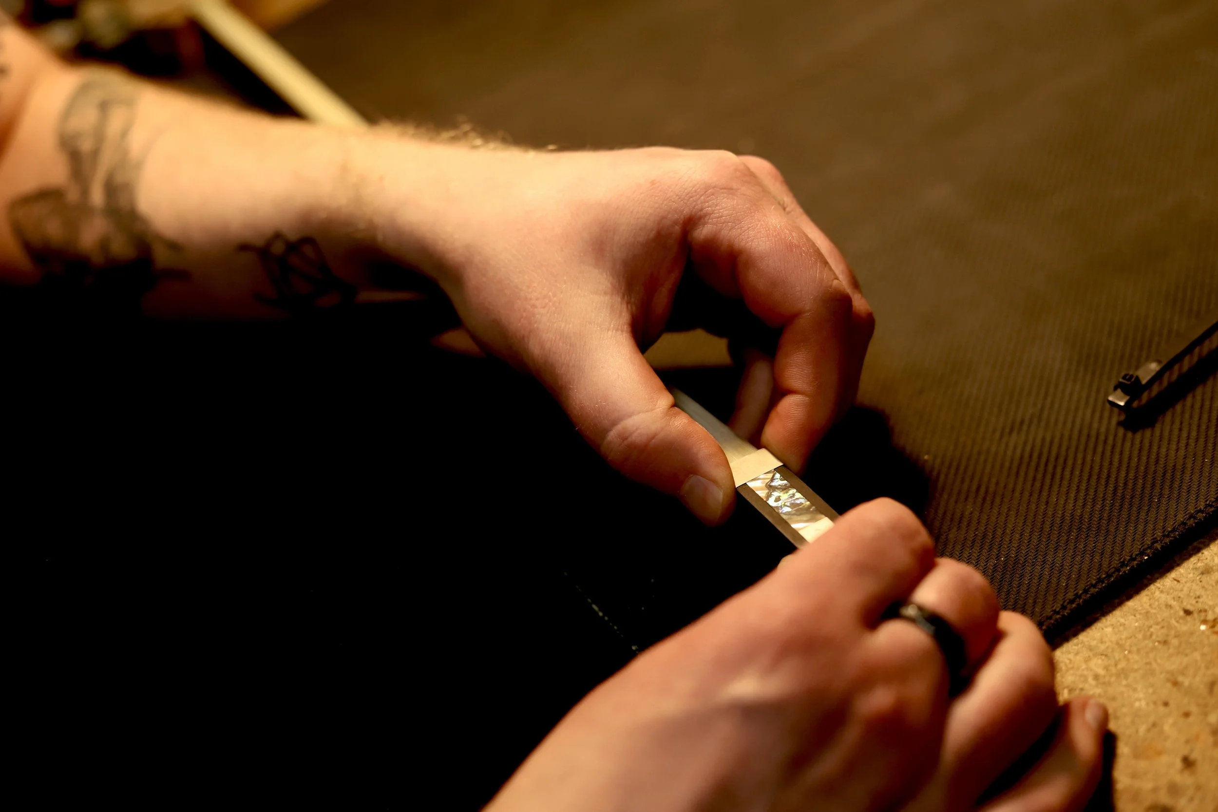 A person's hands holding a violin bow at the base, displaying the intricate mother of pearl slide against a dark surface.