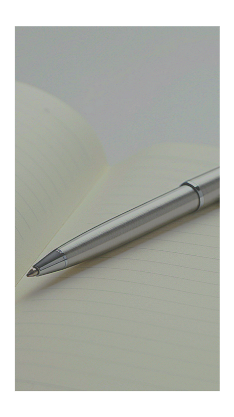 A silver ballpoint pen resting on an open, lined notebook with blank cream-colored pages.