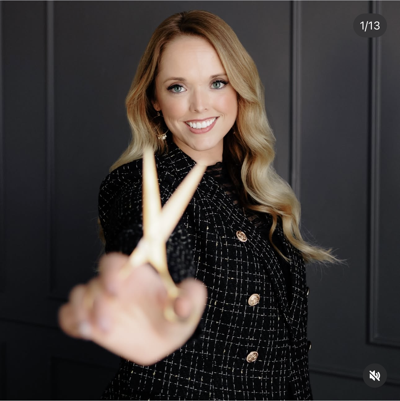A woman with long blonde hair and blue eyes smiling in a black checkered blazer, making a peace sign with her hand towards the camera. Scalp health for stylists.