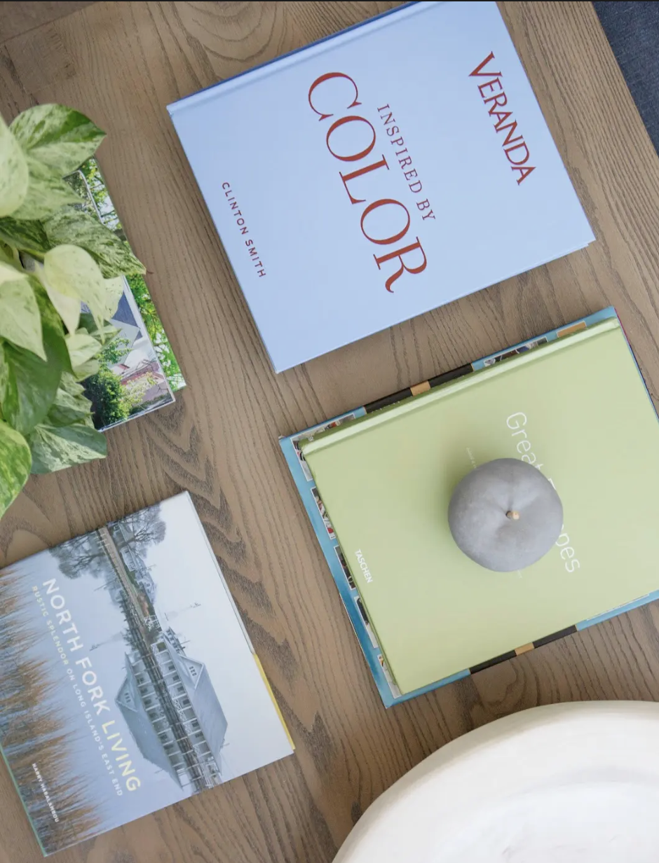 Books about Vermont, North Fork Living, and Green Gables, a plant, and a candle on a wooden table.