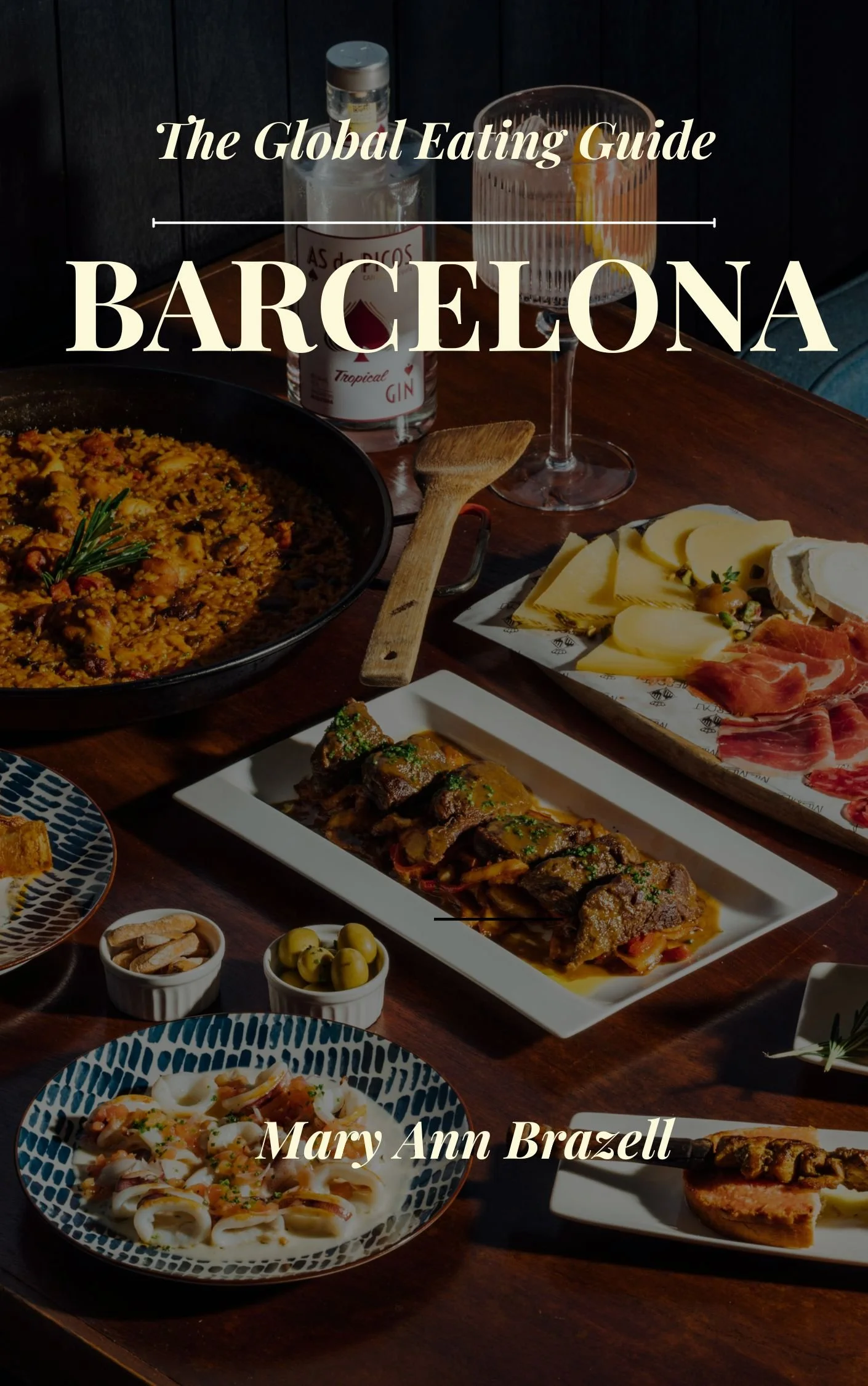 A table filled with various Spanish dishes, including pasta, grilled meat, cheese, cured meats, olives, and a drink, in a cozy dining setting.