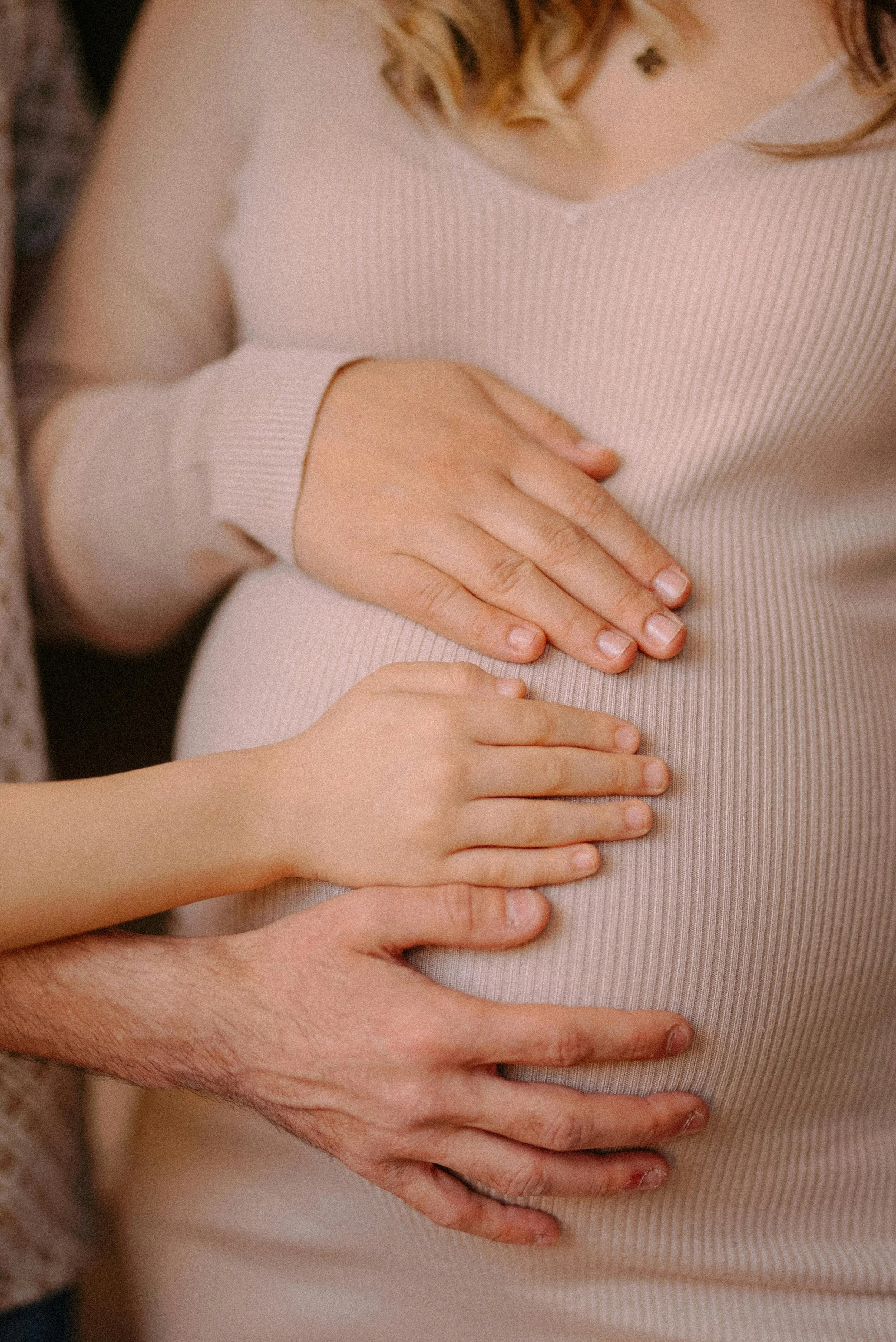 Multiple hands, including a pregnant woman's, gently resting on her baby bump, symbolizing pregnancy and support.