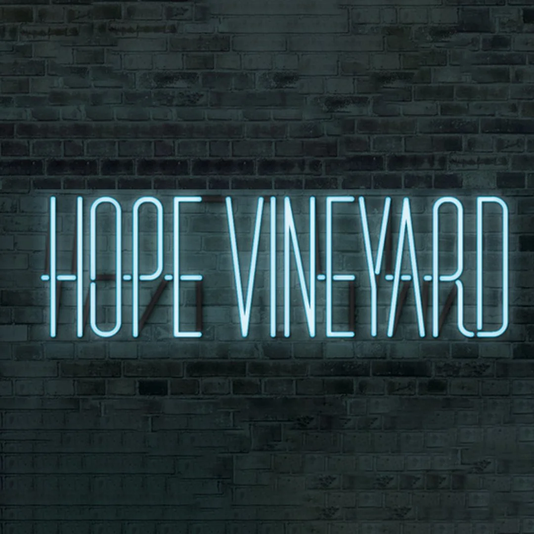 Neon sign on brick wall that reads 'Hope in Vino Veritas' in blue letters.