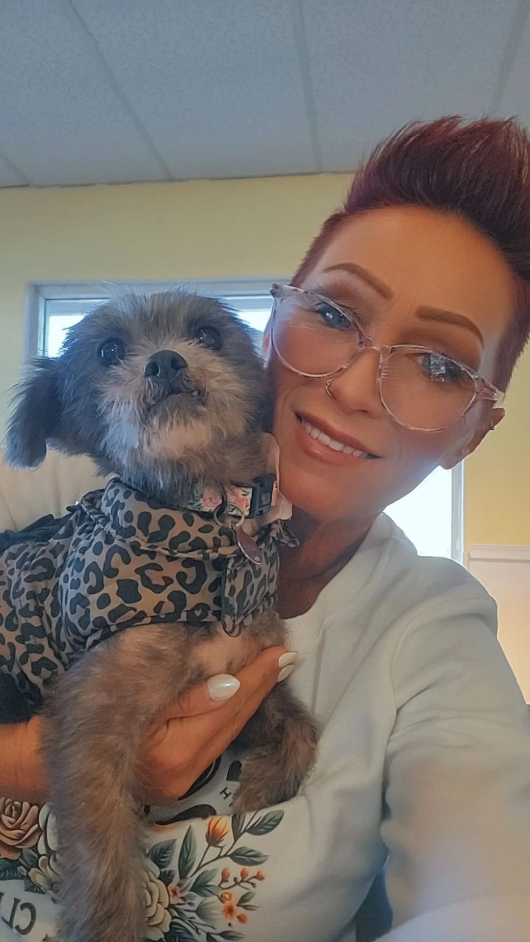 Wendy, Lead Pet Groomer at Tails and Ales in Hickory, NC, holds one of her geriatric rescue Shih Tzus and smiles as she takes a selfie in the seating area of the bar.